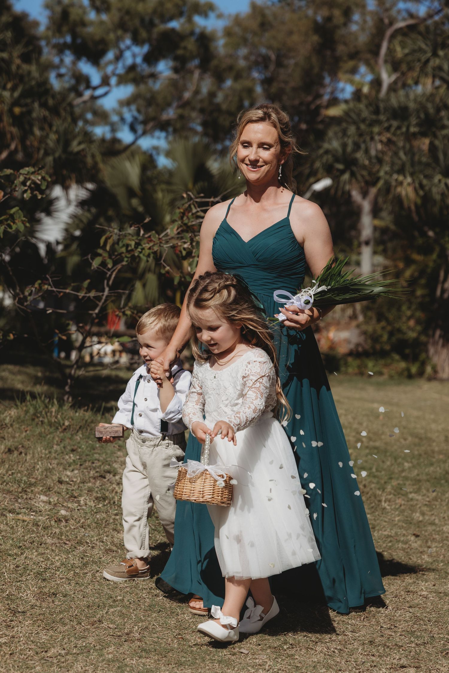 Children in formal attire playing with flower baskets on grassy lawn at wedding.