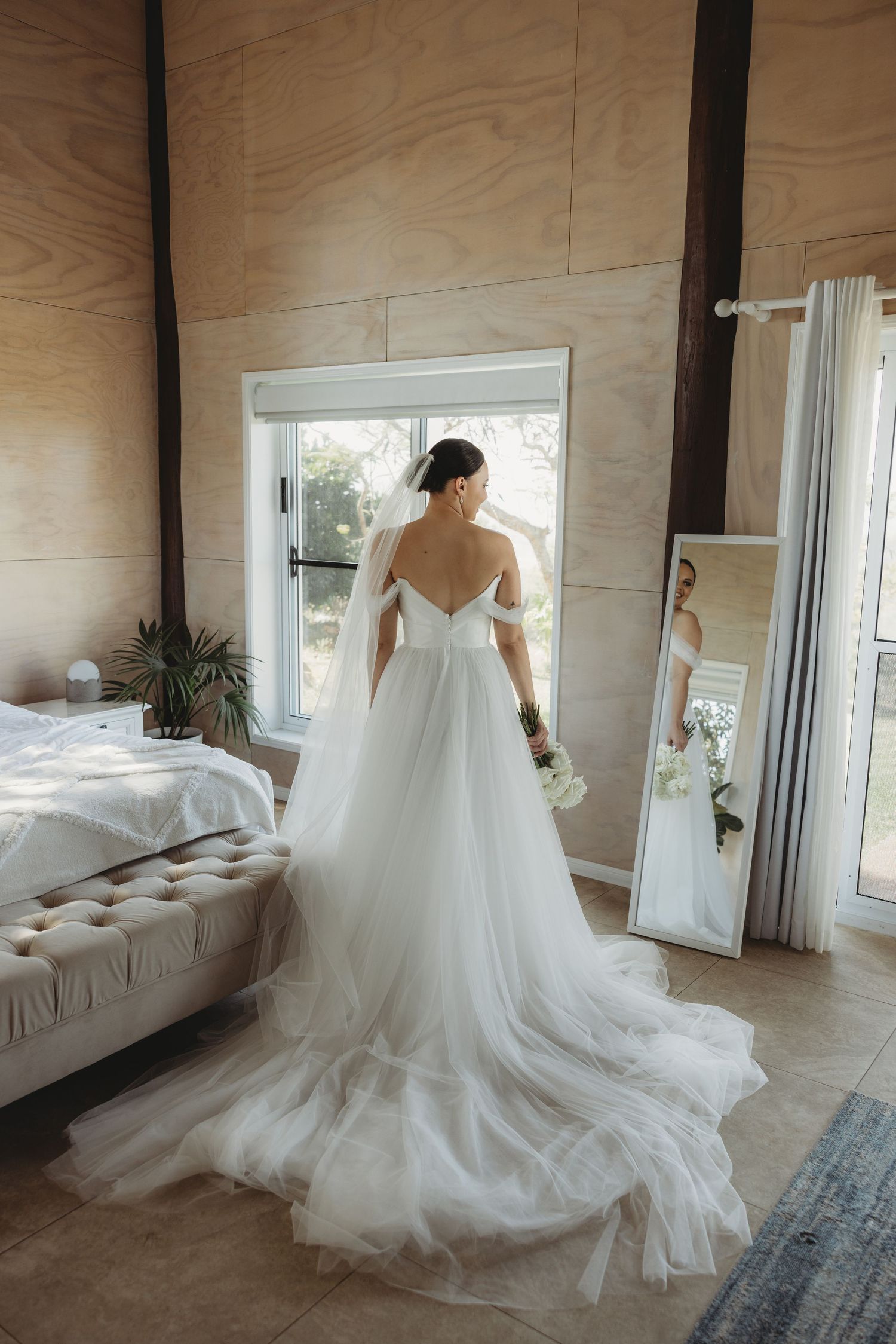 A stunning white wedding dress with a flowing train displayed in a room with wooden walls and natural lighting.