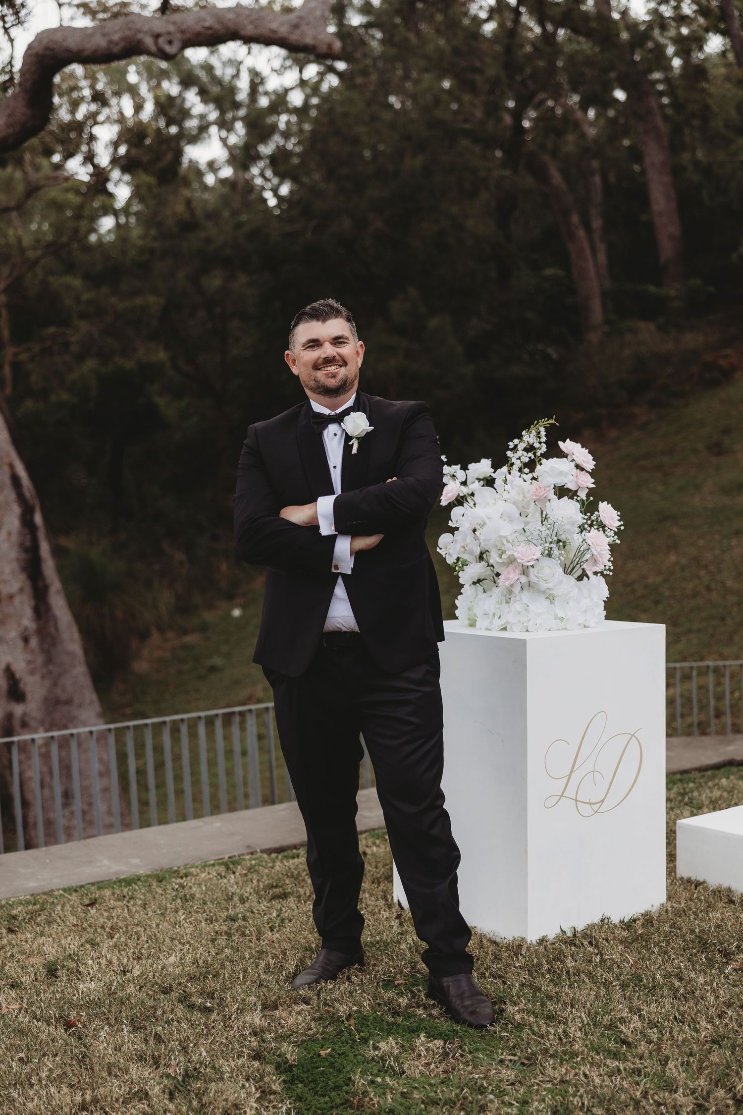 An elegant wedding setup with a white pedestal and floral arrangement against a natural outdoor backdrop.