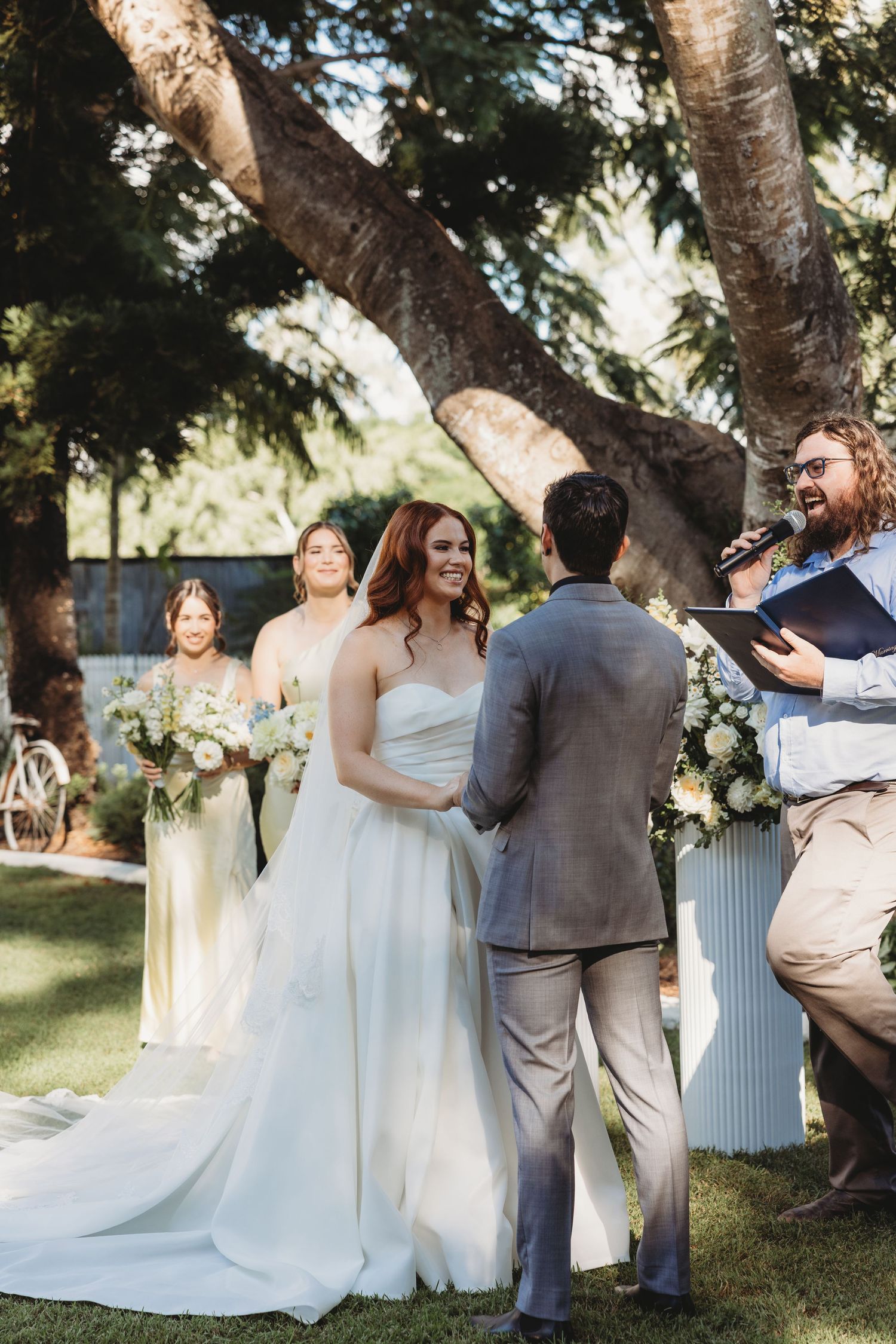 Wedding party members gather under trees during an outdoor celebration.