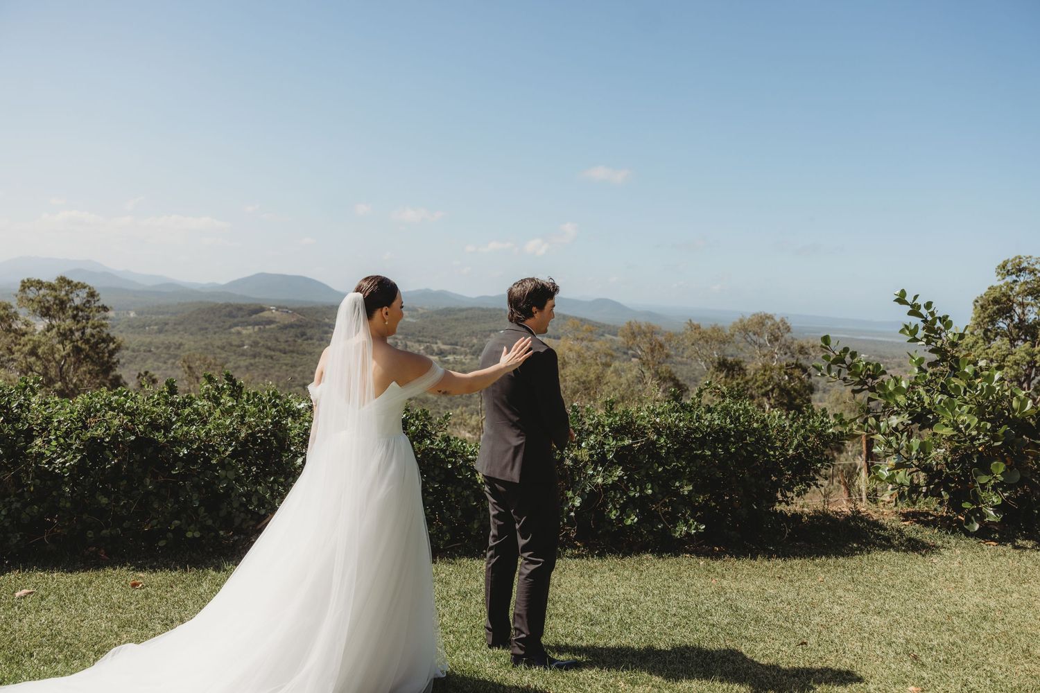 A wedding couple shares an intimate moment on a hilltop overlooking a scenic mountain landscape.