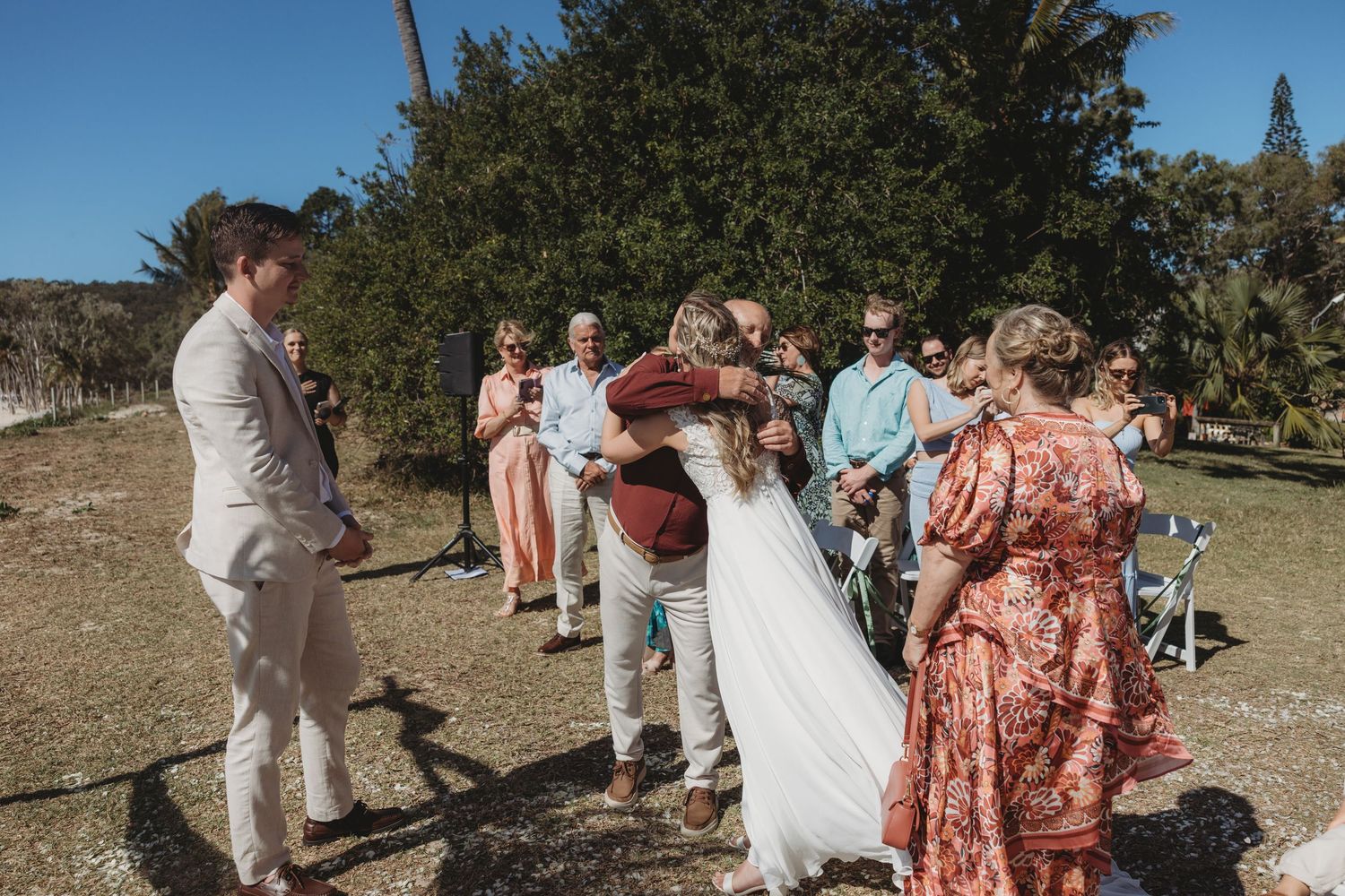 Wedding ceremony guests mingling on grassy area near the beach.
