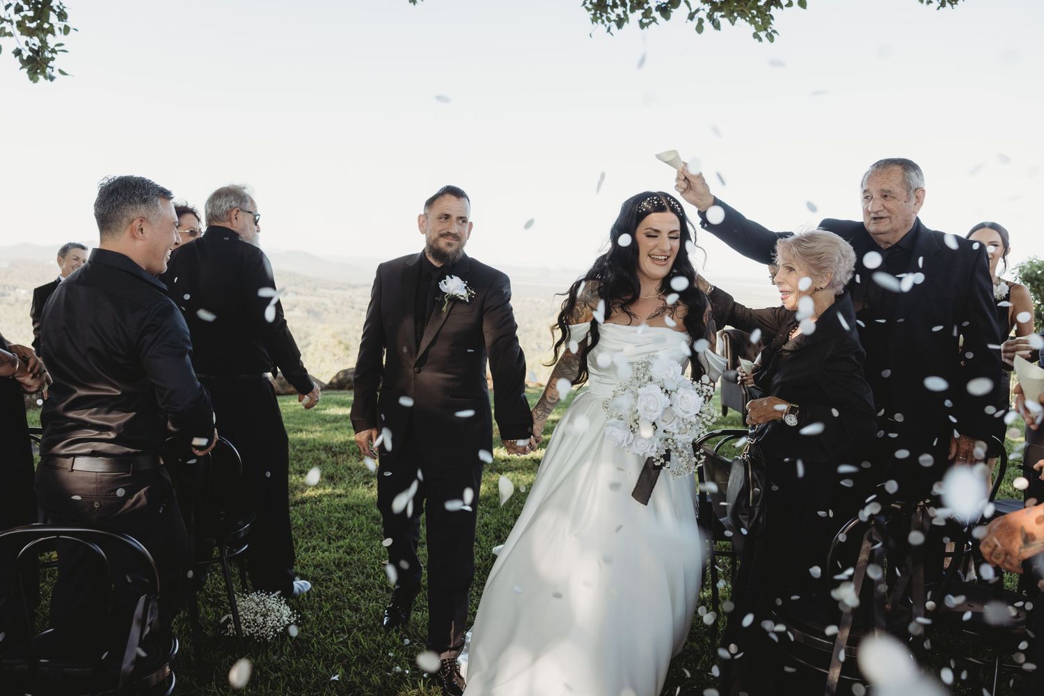 Wedding party stands outdoors in a garden setting with confetti floating through the air during a celebration.