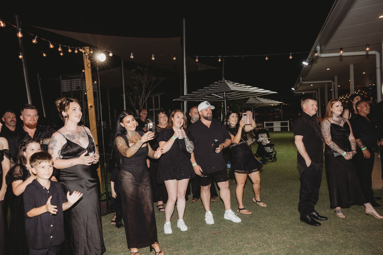 Wedding reception guests dancing under string lights at an outdoor evening celebration.