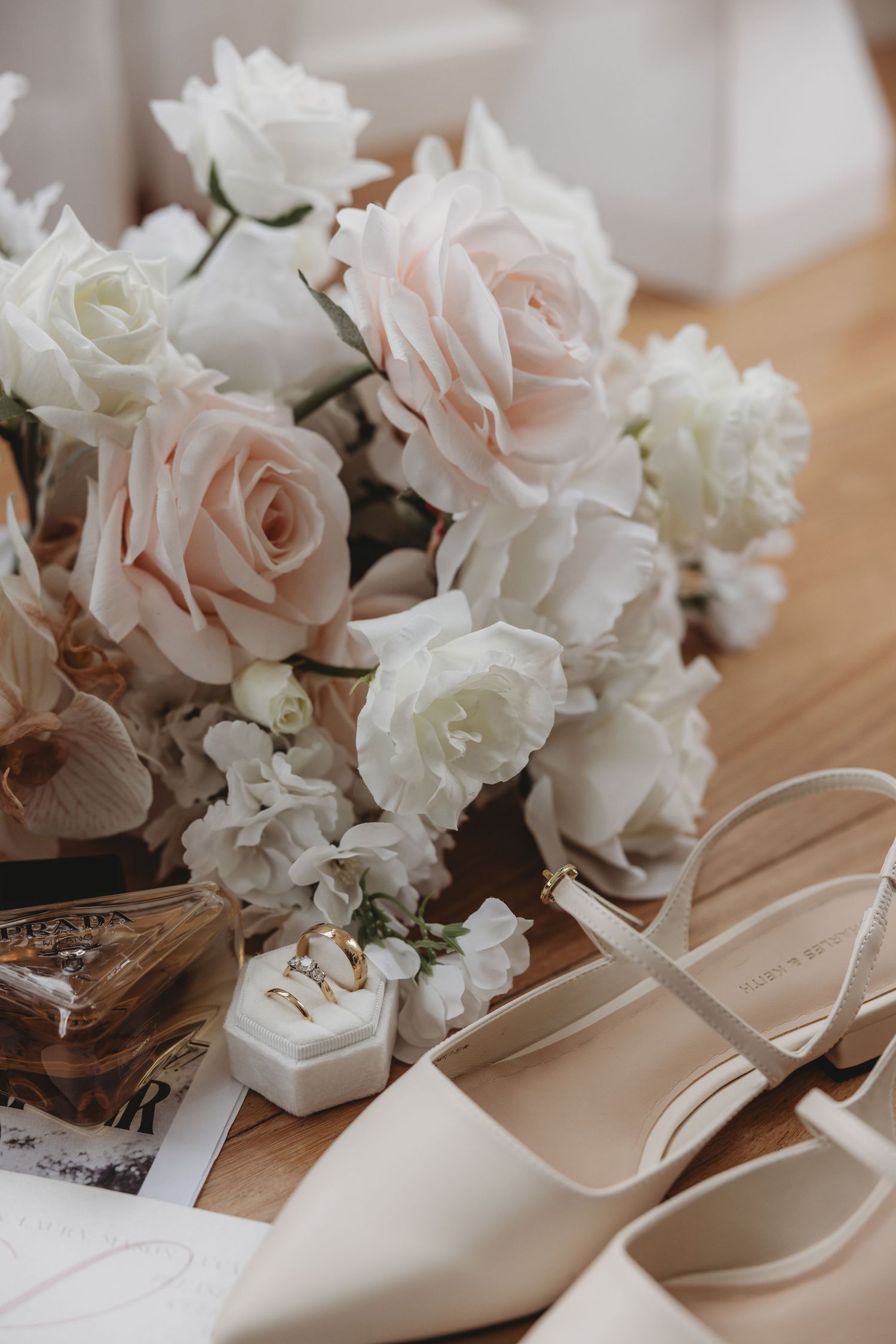 Wedding details featuring pale pink and white roses alongside elegant bridal shoes on wooden surface.
