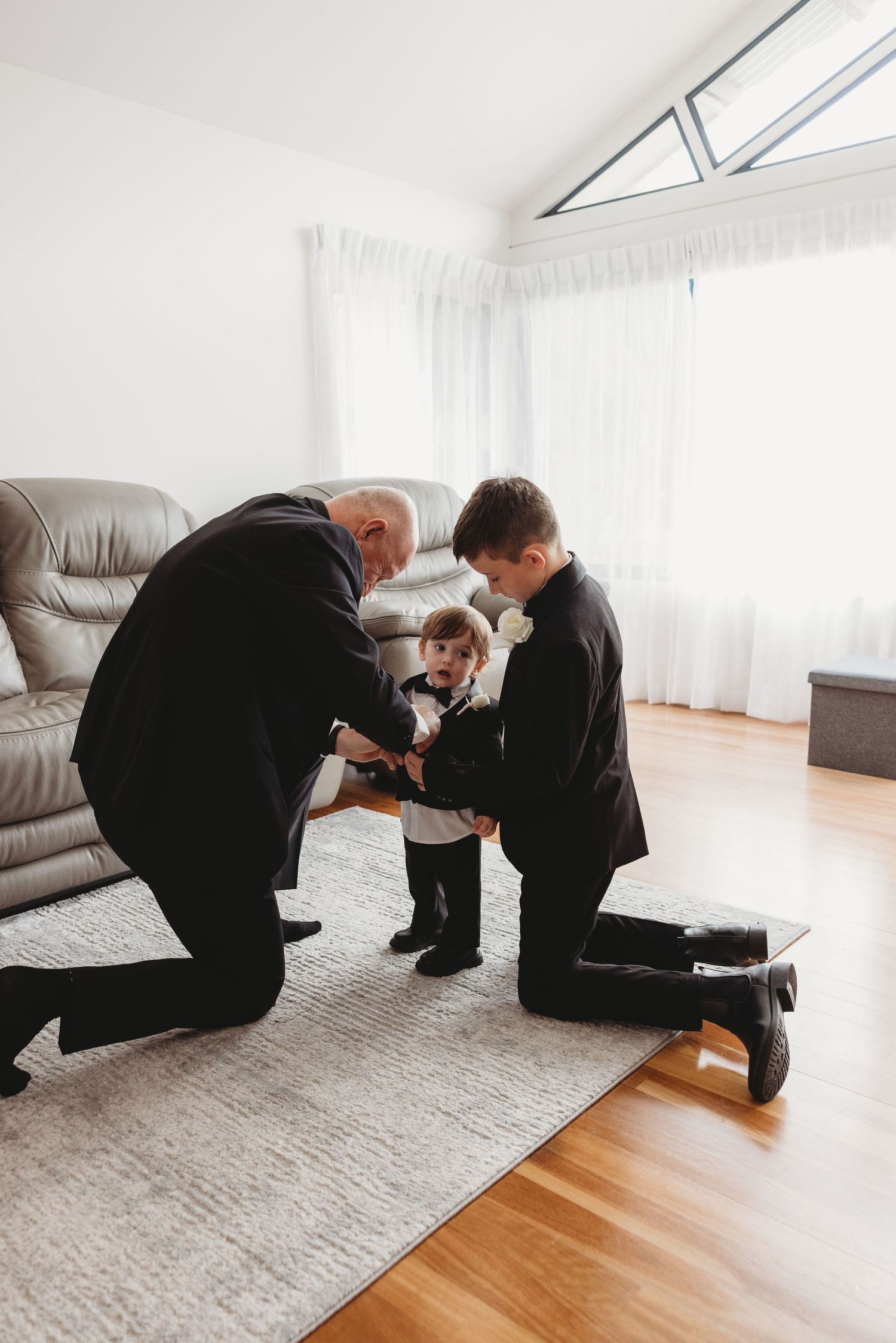 A touching moment as two people help a small child get dressed in a bright living room with hardwood floors.