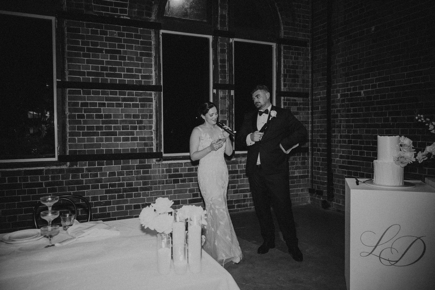Black and white photograph of people walking along a brick wall at night with dramatic shadows.