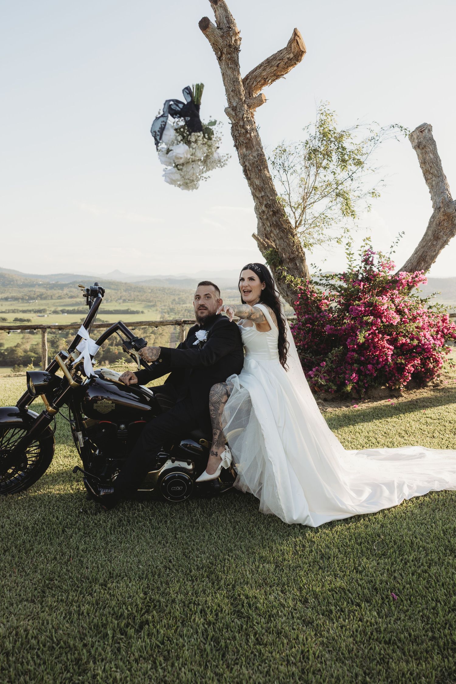 A wedding photoshoot with a motorcycle on a grassy hill with mountains in the background.