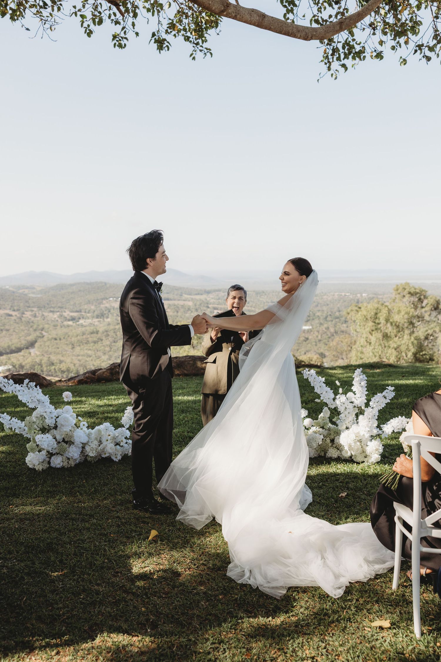 Candid wedding moments captured outdoors with white floral decorations and scenic mountain views.