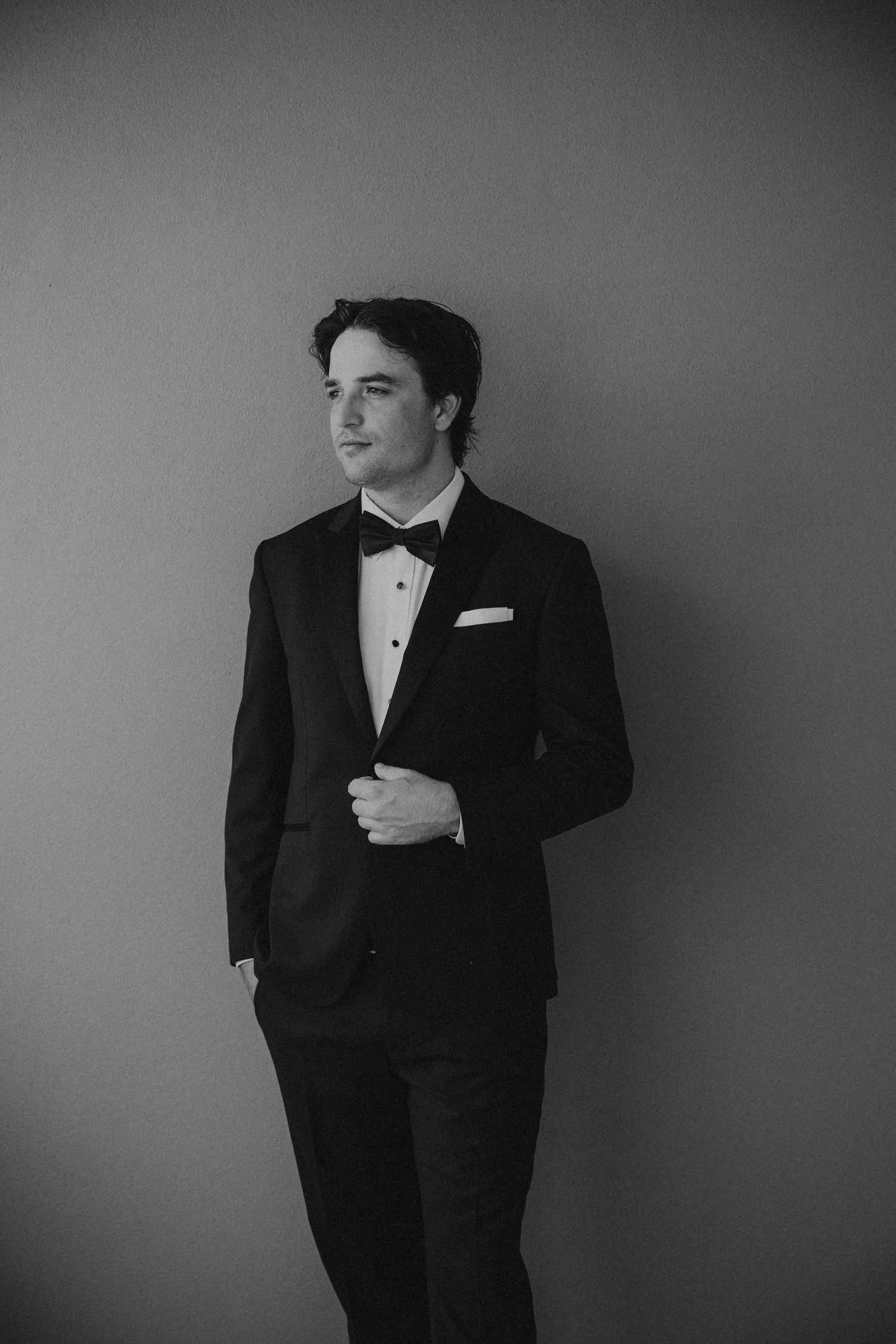 Classic black and white portrait of someone in a tuxedo against a grey background.