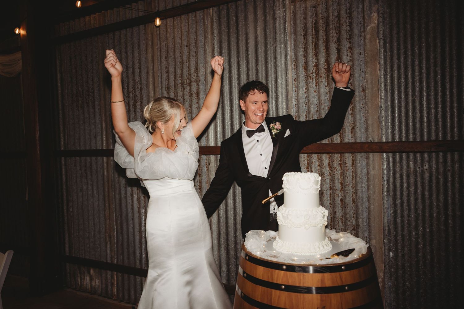 Wedding couple cutting their traditional white tiered cake at rustic barrel display.