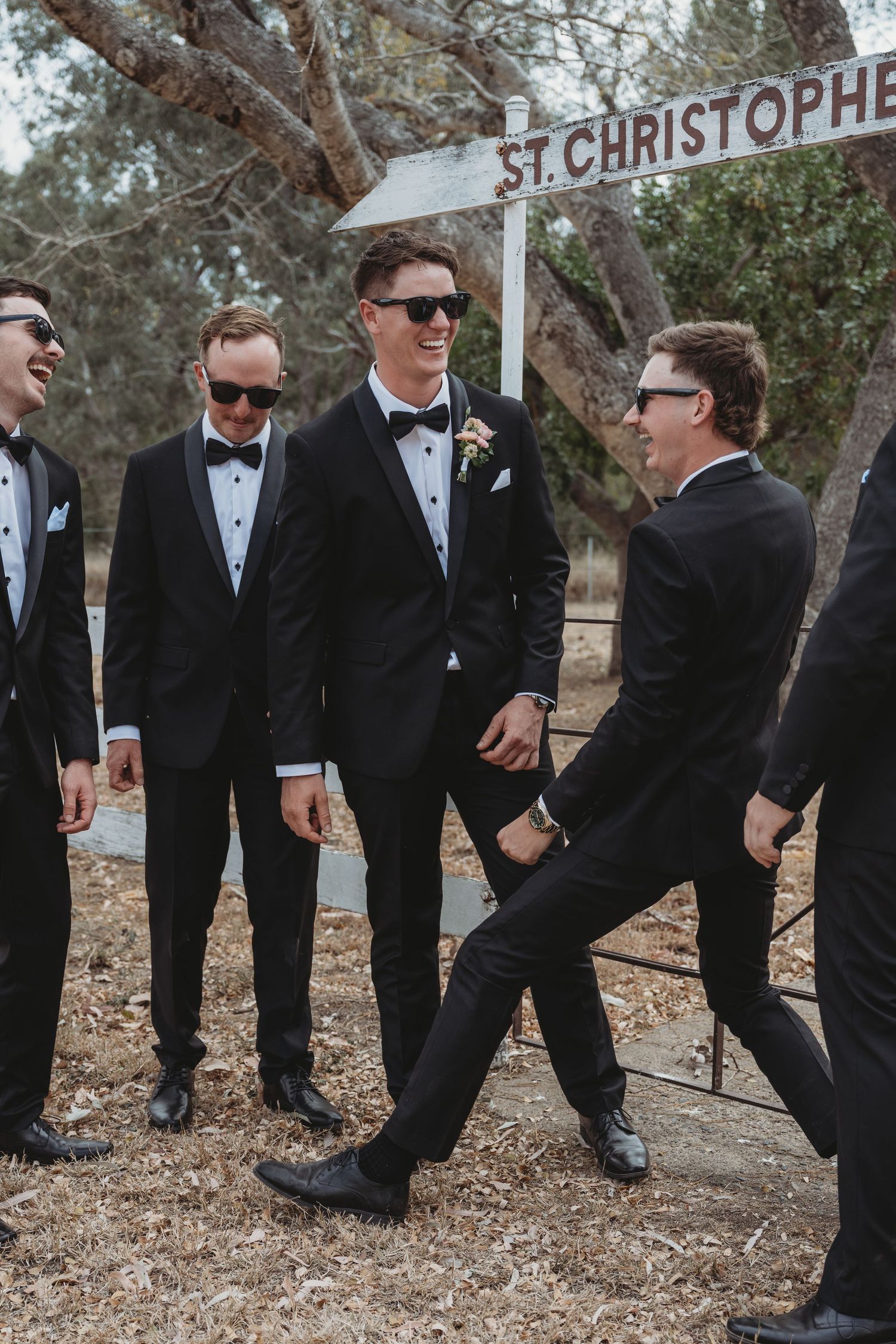 Groomsmen in tuxedos posing playfully outdoors.