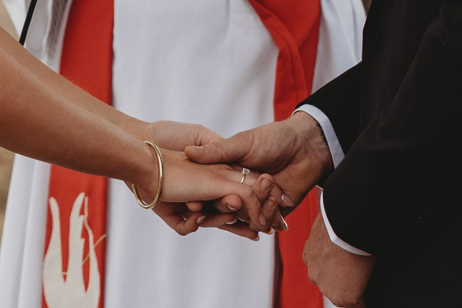 Close-up of hands exchanging rings during an outdoor wedding ceremony.