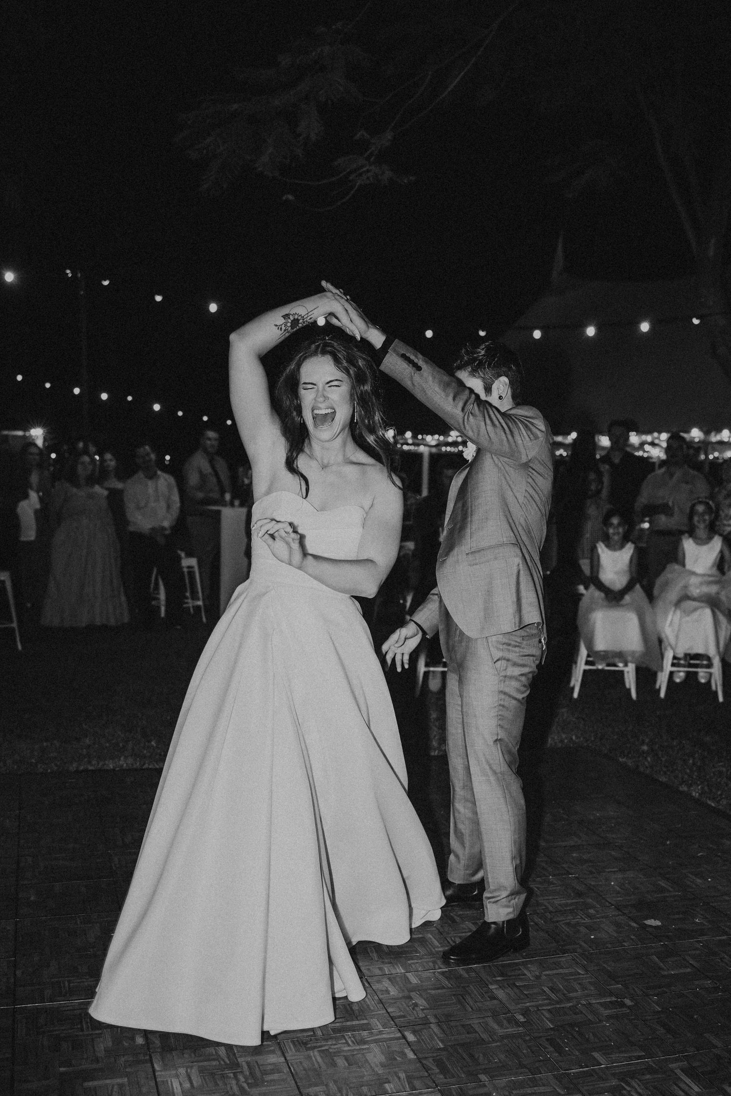 Wedding guests dancing and celebrating on a brick patio under string lights at night.