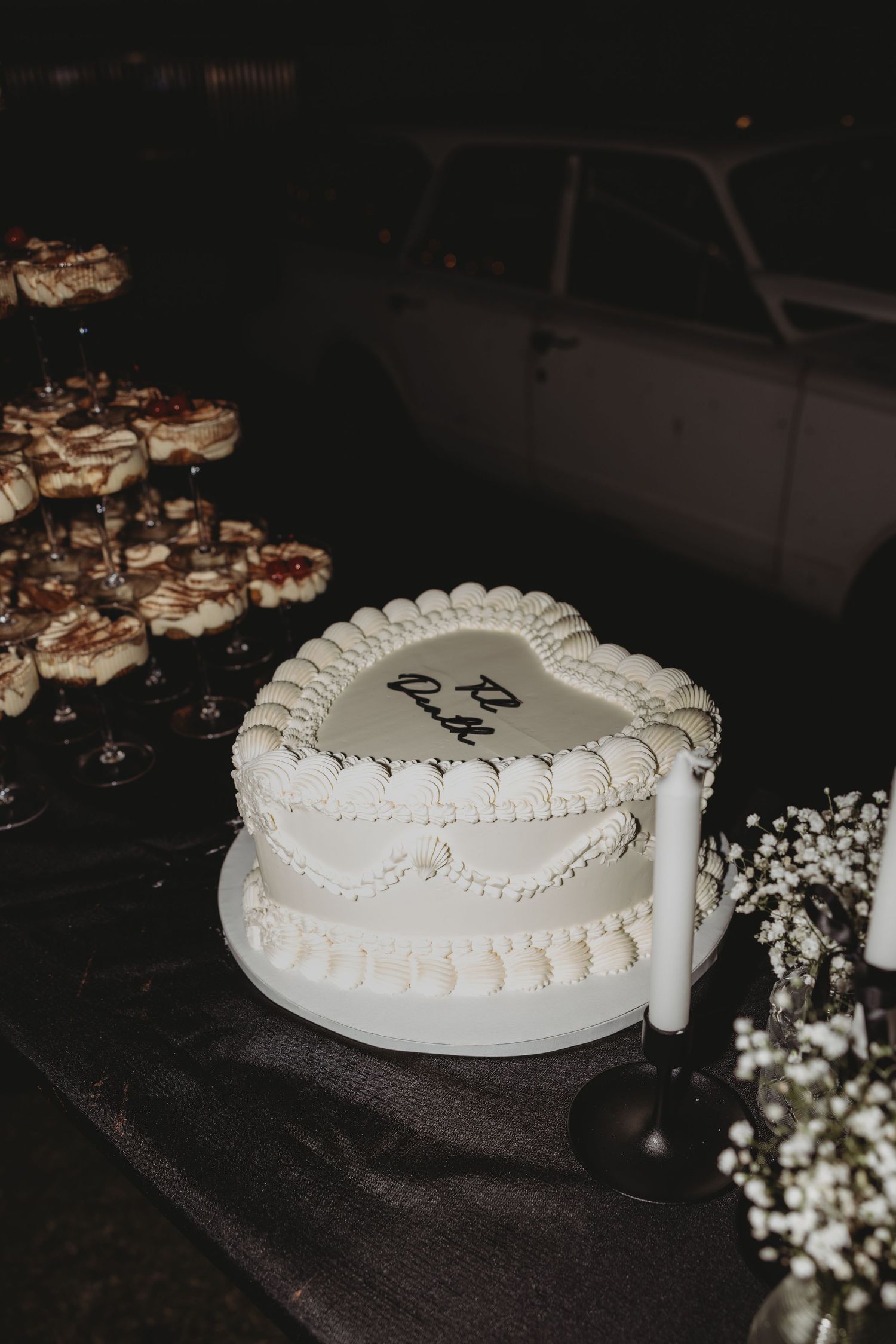 White heart-shaped wedding cake with delicate piped details on a dark tablecloth.