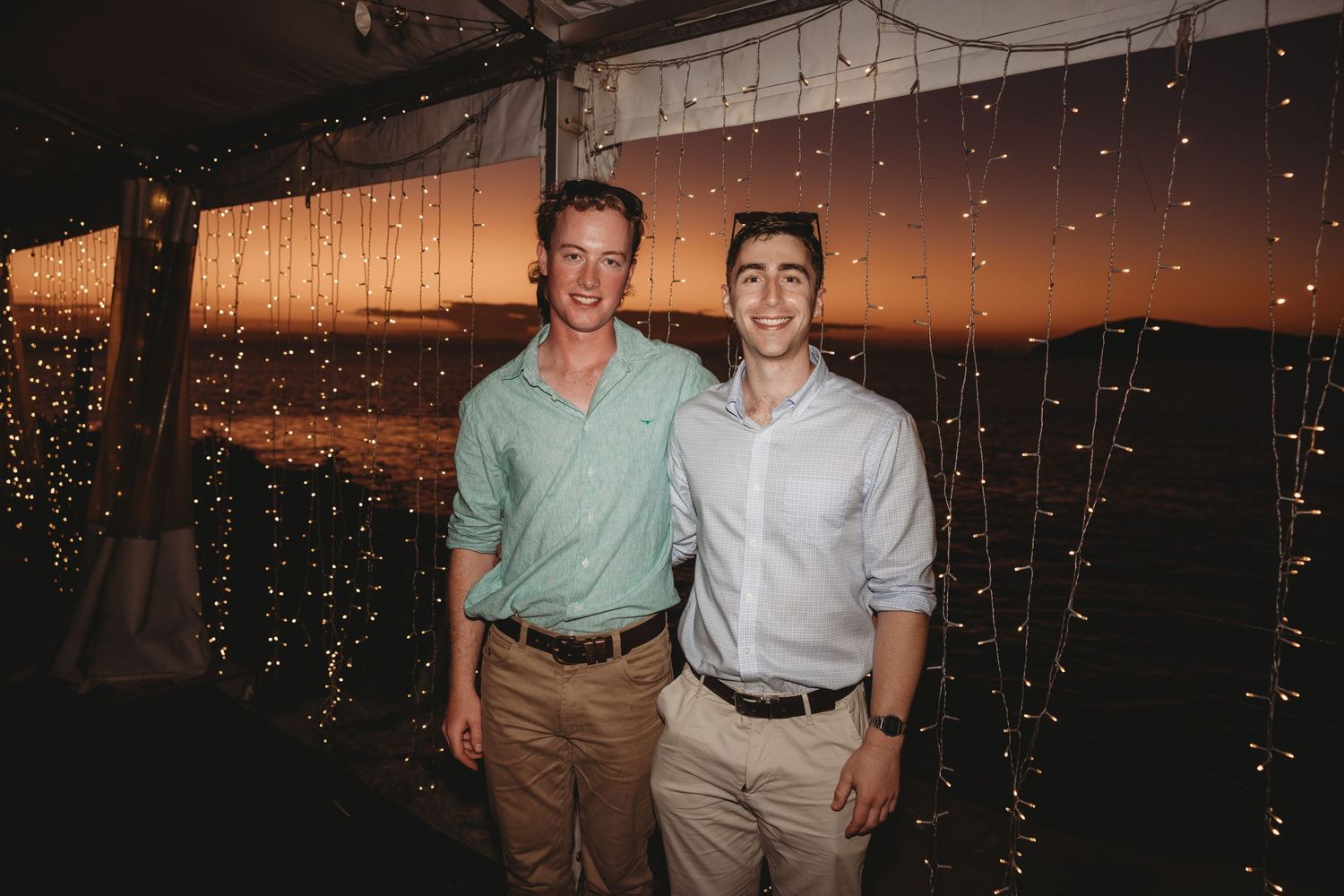 A romantic wedding reception under string lights at sunset with guests seated at tables.