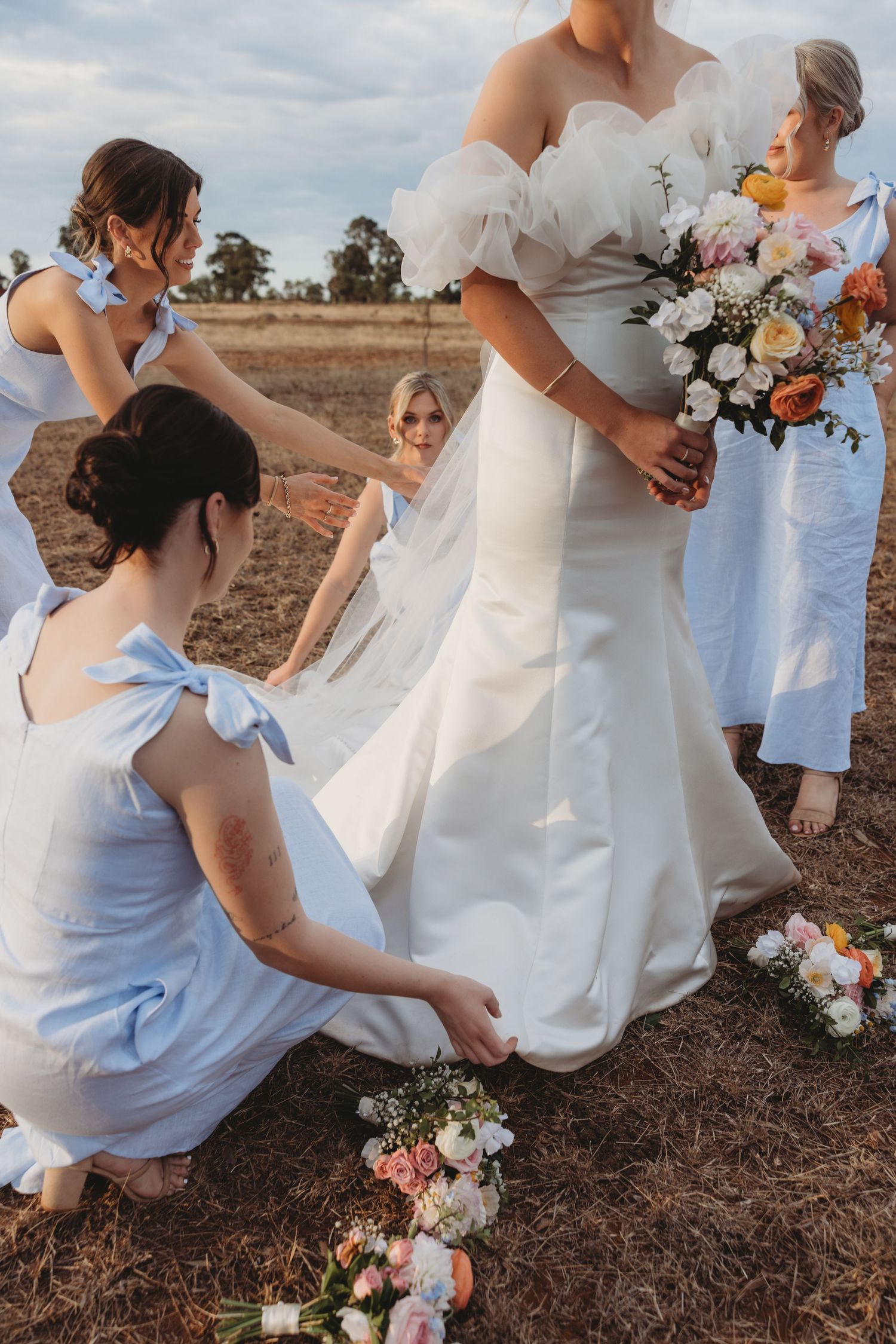 Close-up of wedding party dresses and bouquets during an outdoor countryside photoshoot.