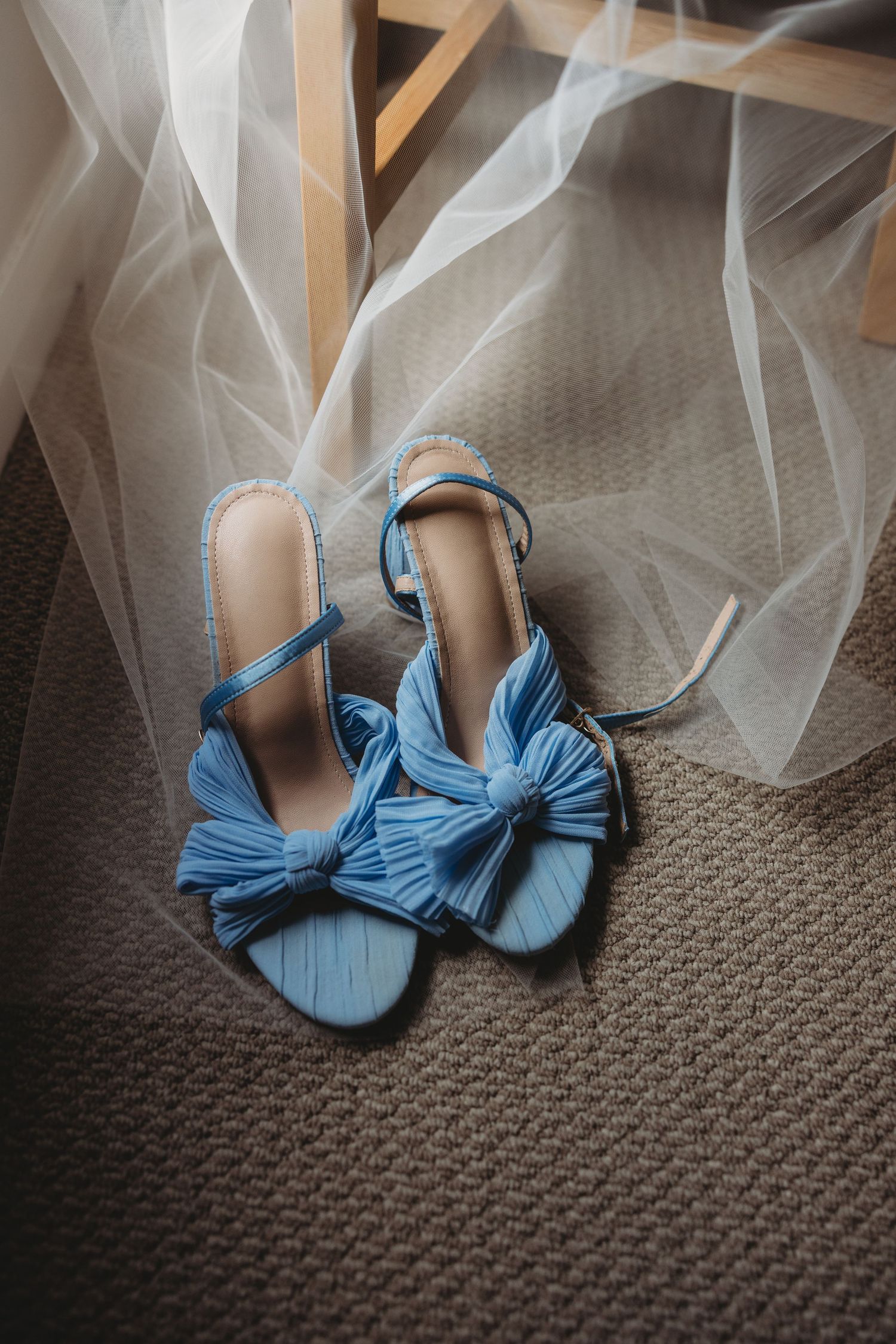 Blue bow wedding shoes with tulle veil on textured carpet.