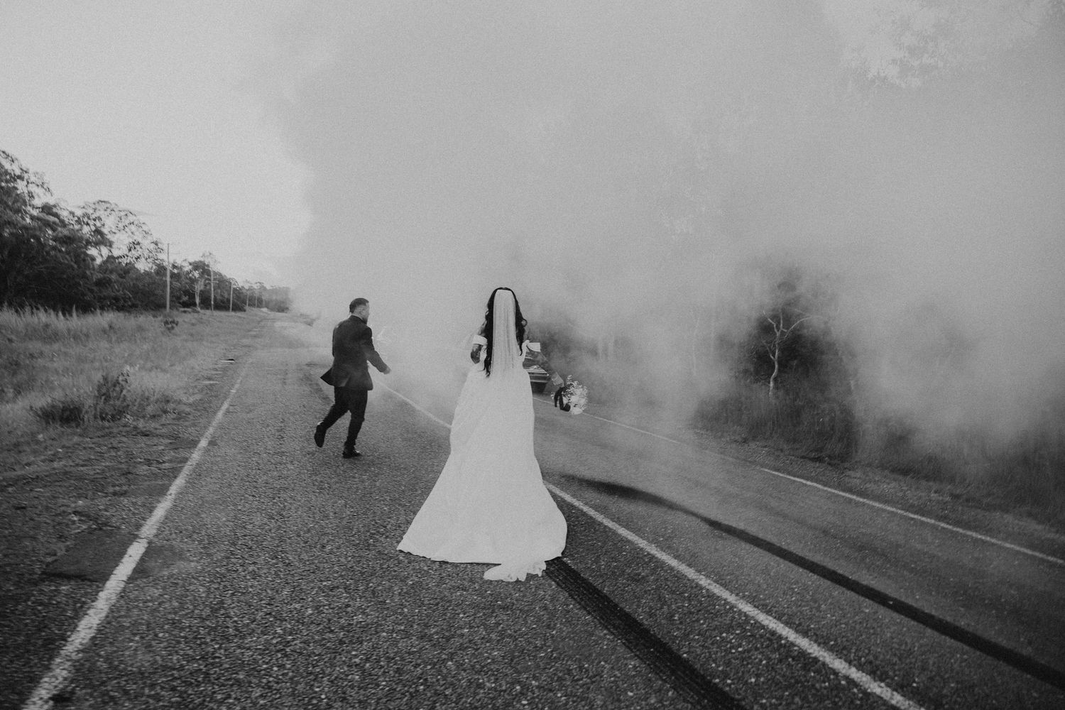 Artistic black and white photo of couple with smoke effects on rural road.