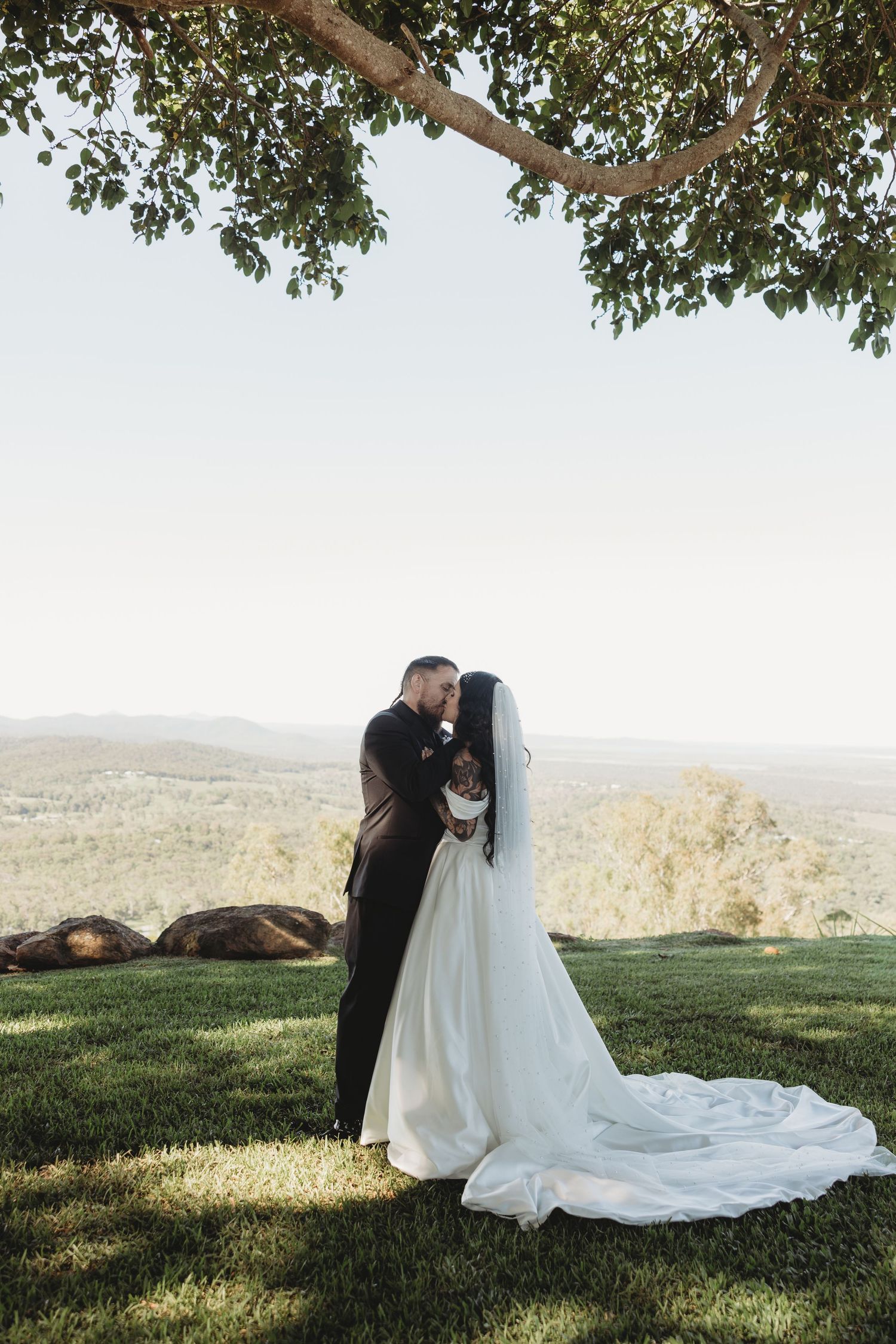 Romantic wedding portraits on a grassy hilltop with scenic countryside views in the background.