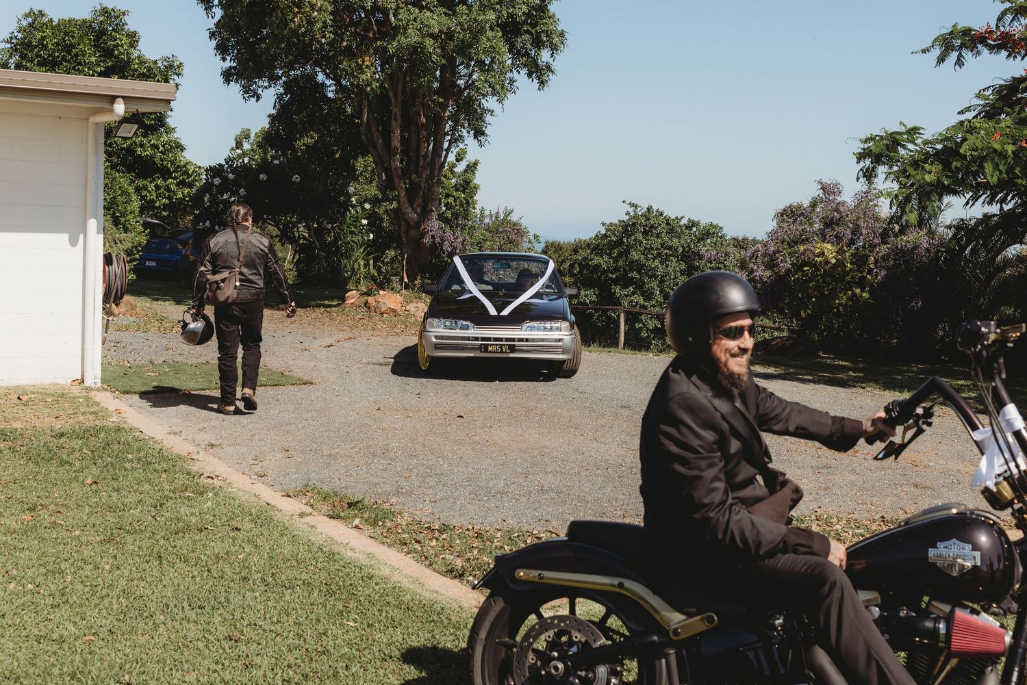 A group of motorcyclists gather at a scenic overlook on a sunny day with trees and parked bikes visible.