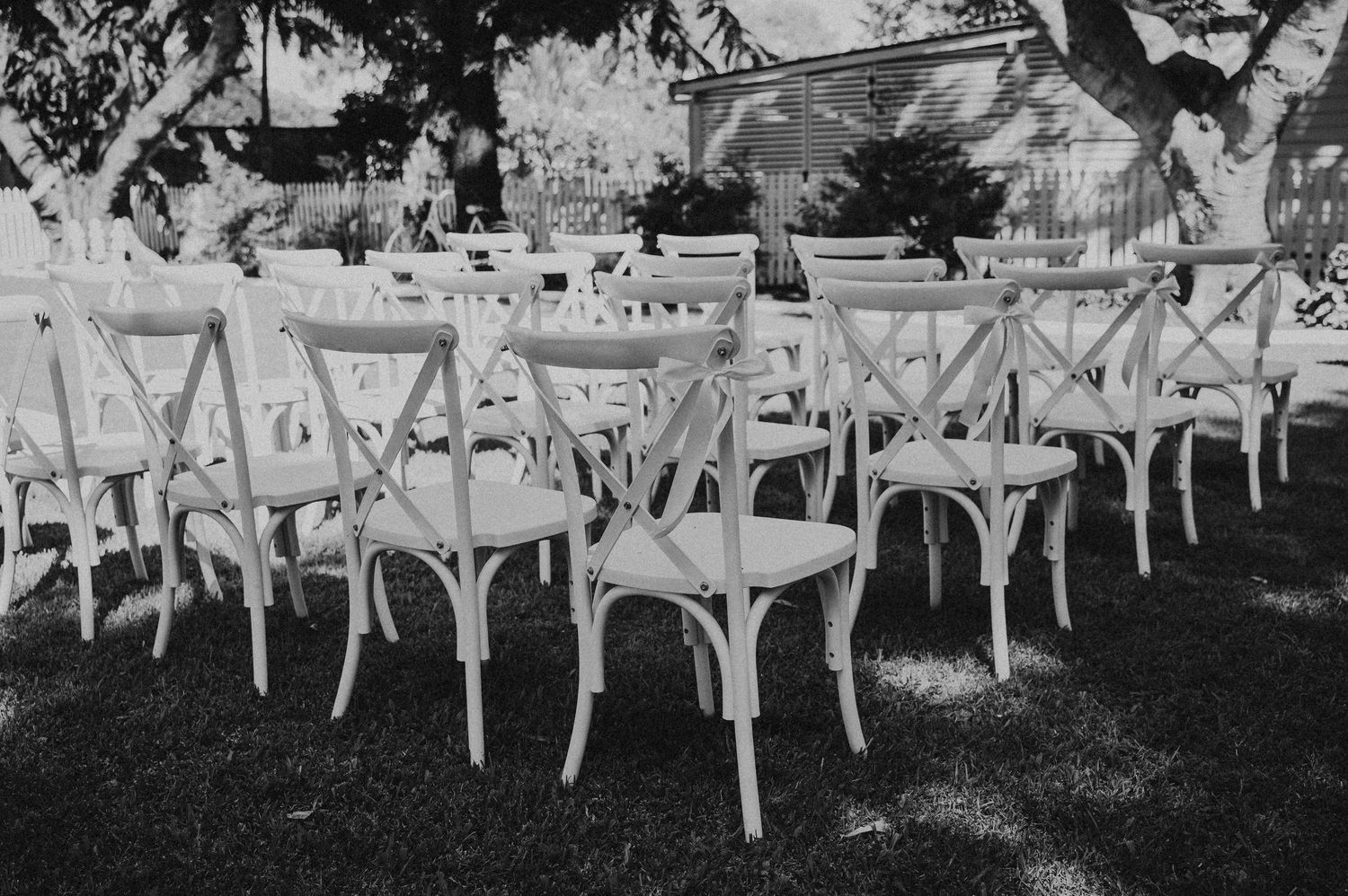Black and white photo of outdoor wedding reception seating with white cross-back chairs St aubins village