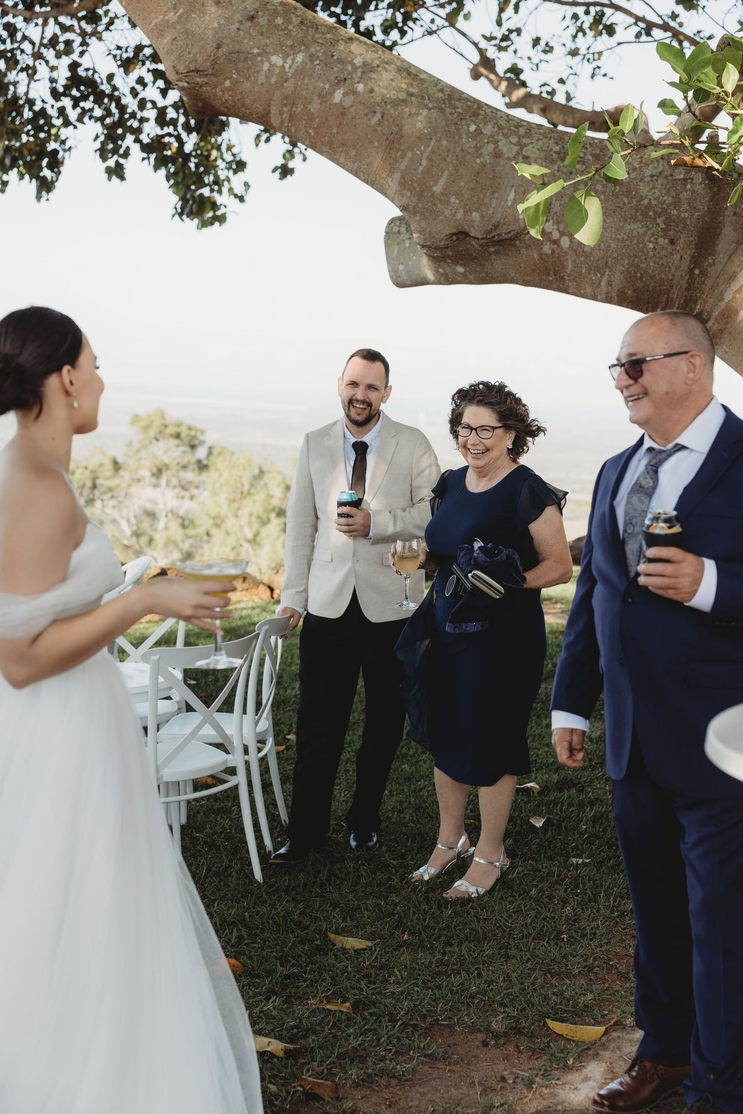 Wedding guests mingle under a large tree during an outdoor celebration.