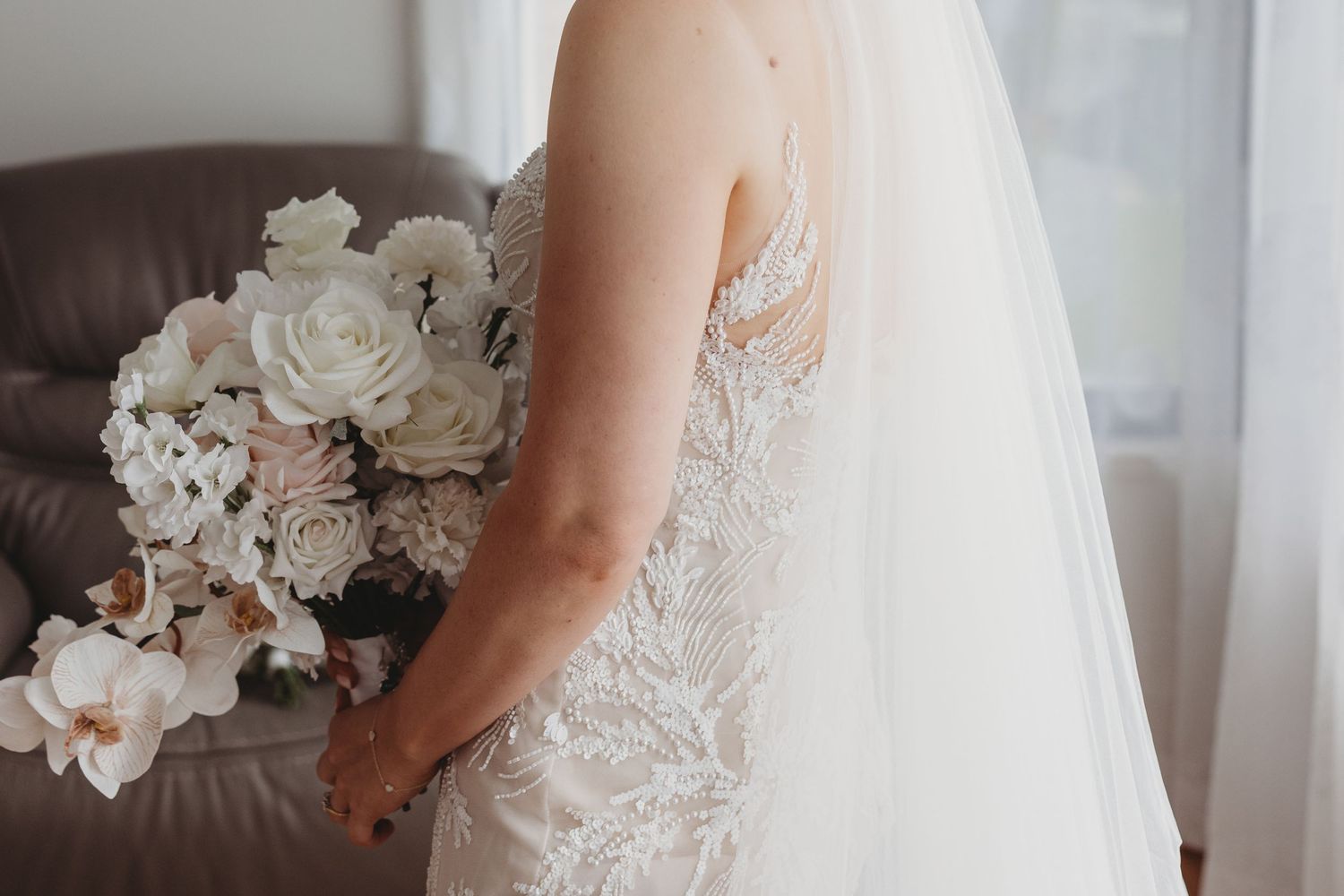 A delicate white wedding dress with lace detailing and veil next to a soft pastel floral bouquet.