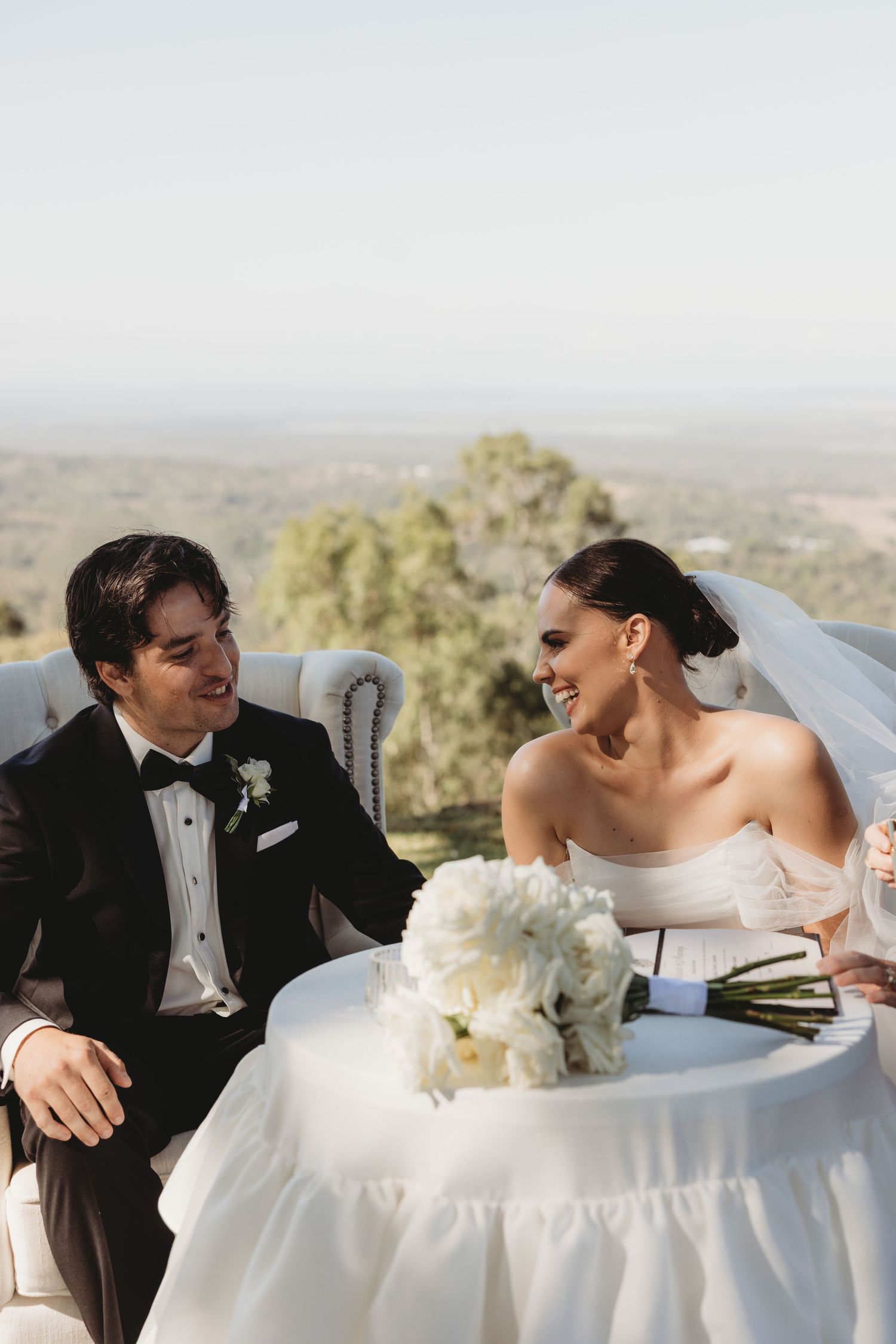 Newlyweds share joyful moments at their reception table with scenic views in the background.