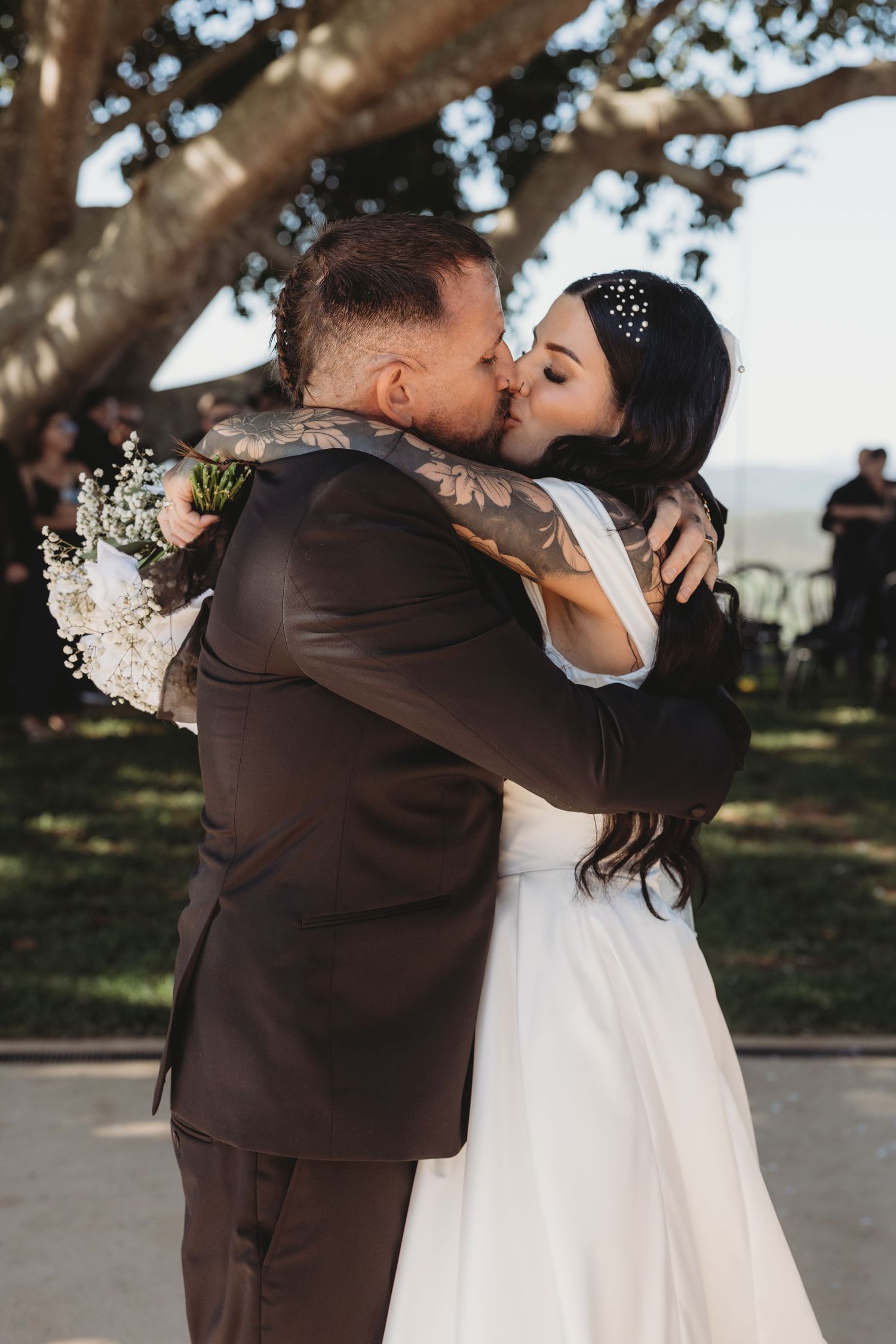 A romantic wedding kiss under a large tree with scenic views.