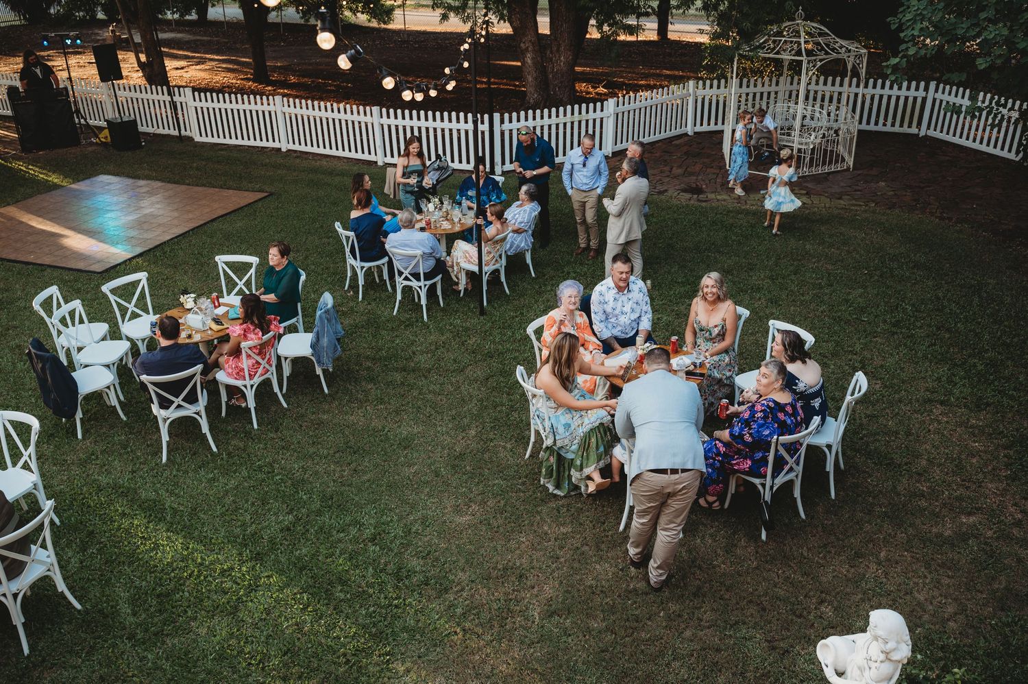 Outdoor wedding reception setup with white chairs arranged on a lawn under string lights.