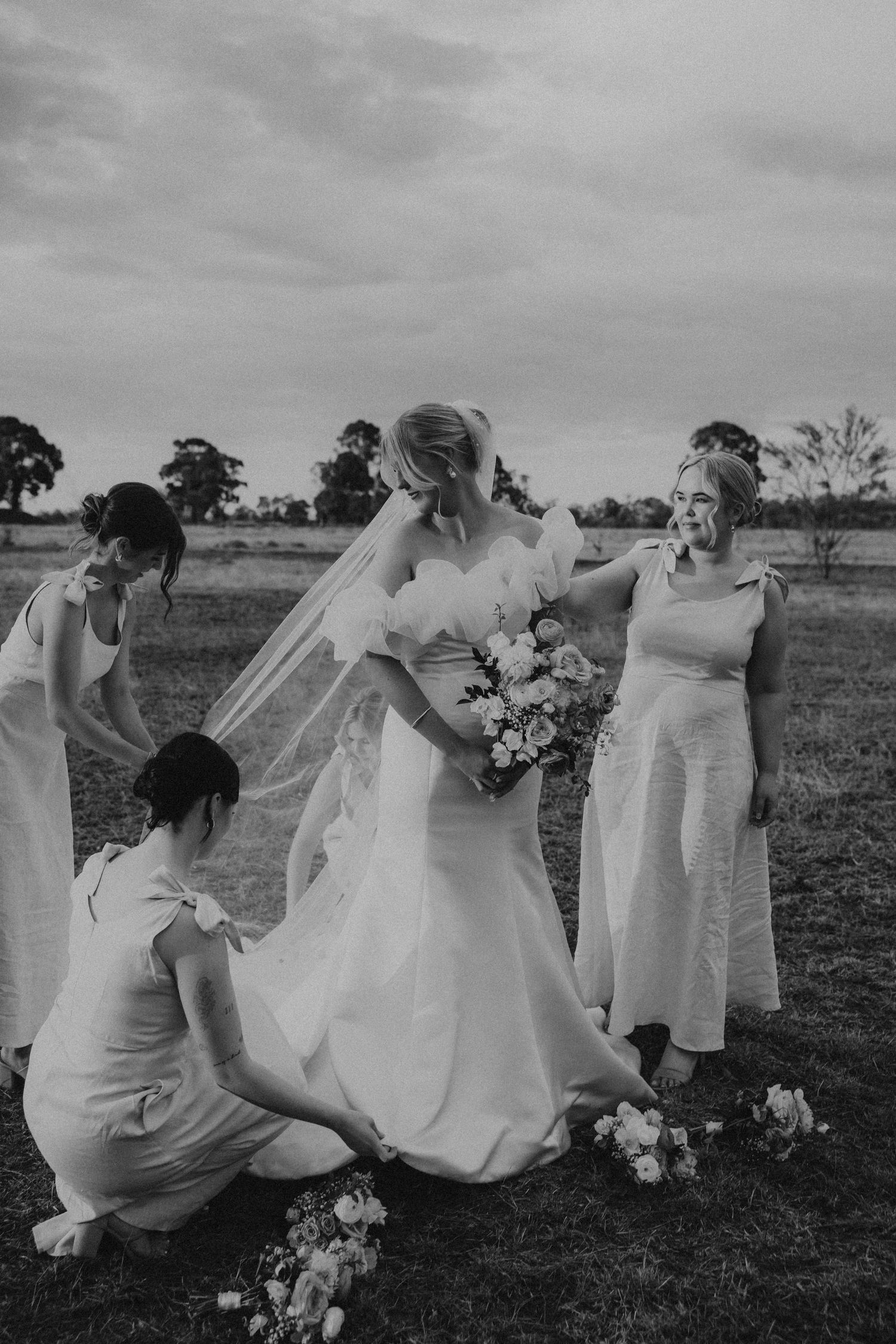 Wedding party in white dresses poses candidly on grass during an outdoor photo session.