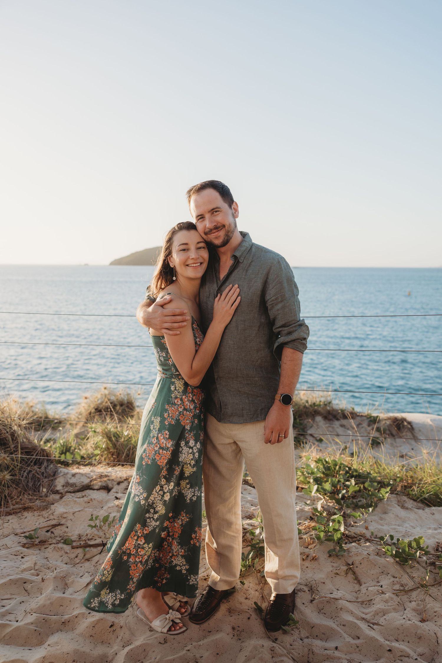 Couple embraces on sandy beach overlook with ocean view at sunset.
