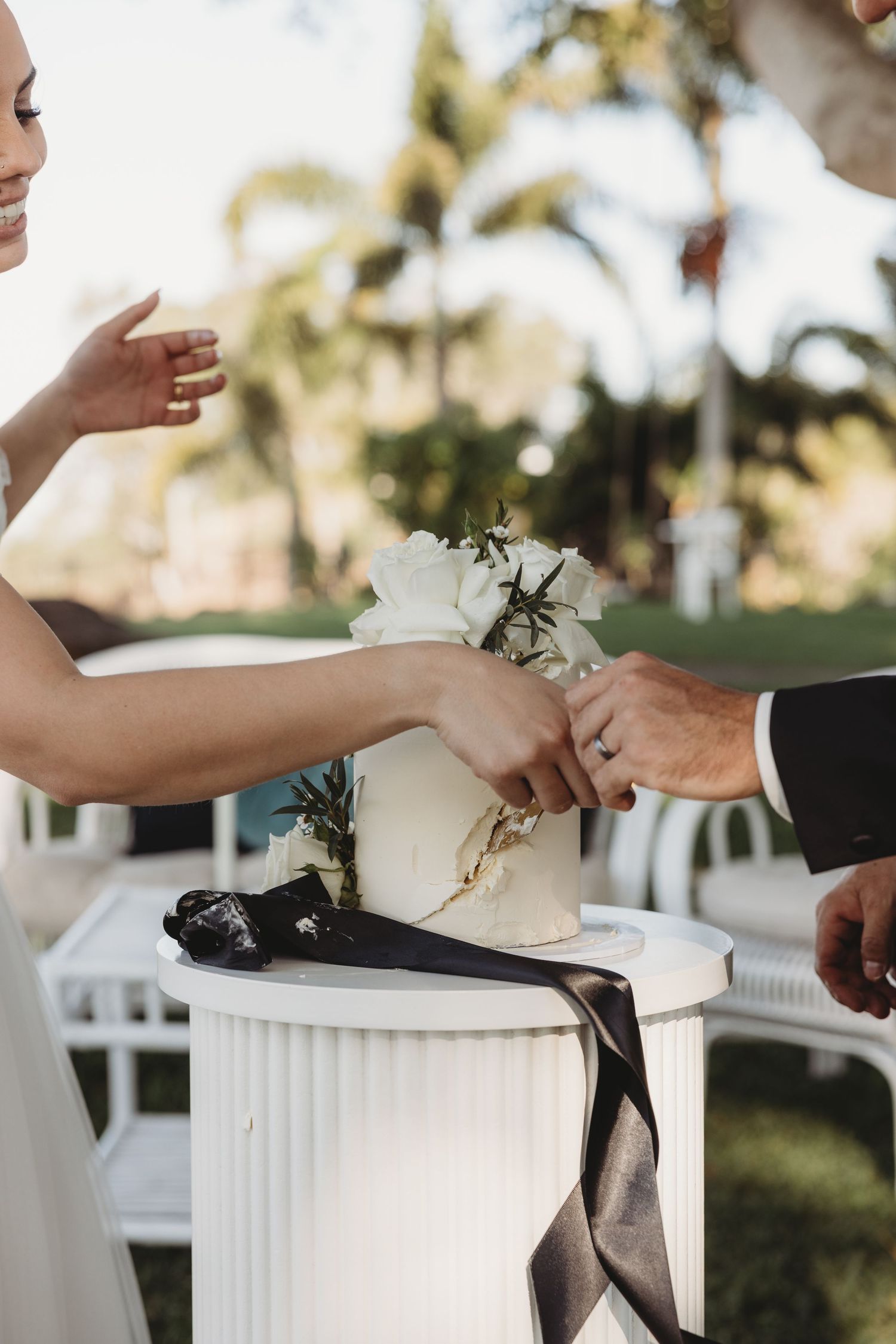 Close-up details of wedding cake cutting with white floral decorations and black ribbon accents.