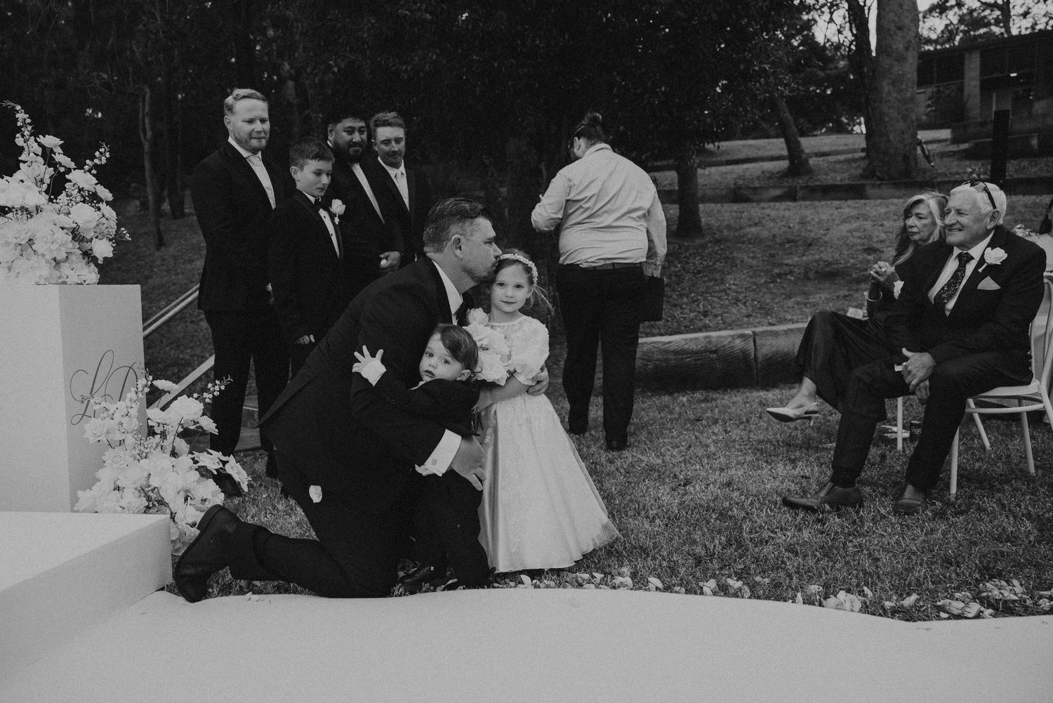 A black and white photo of a wedding party standing together outdoors during a formal ceremony.