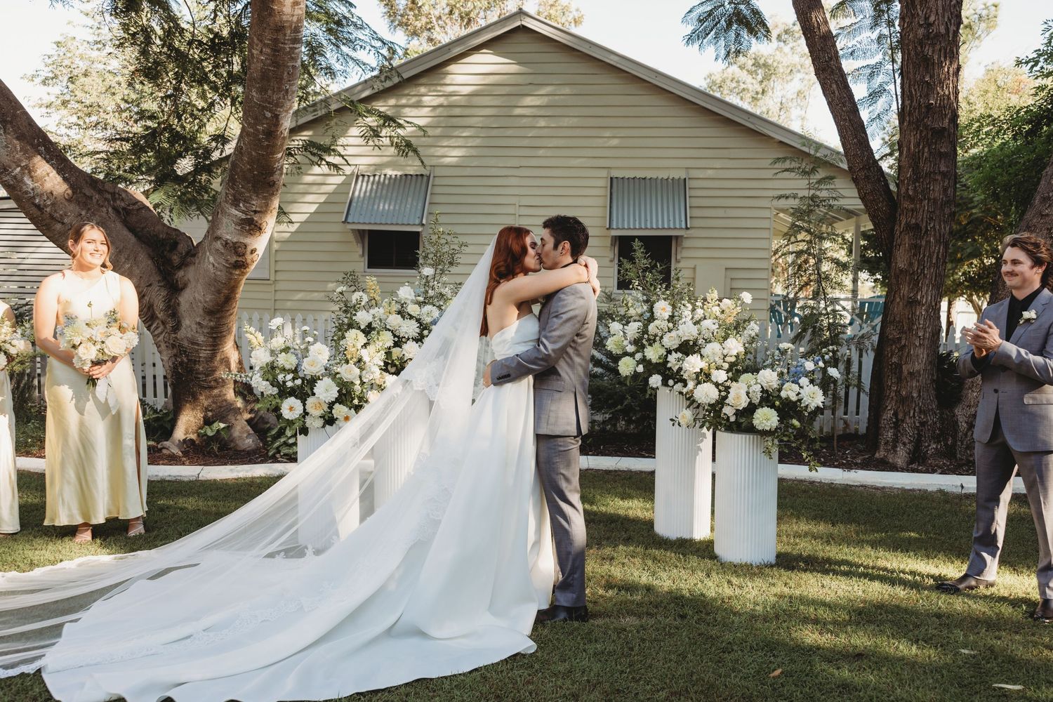 A wedding photo session in front of a traditional house with flowing white dress and floral arrangements.