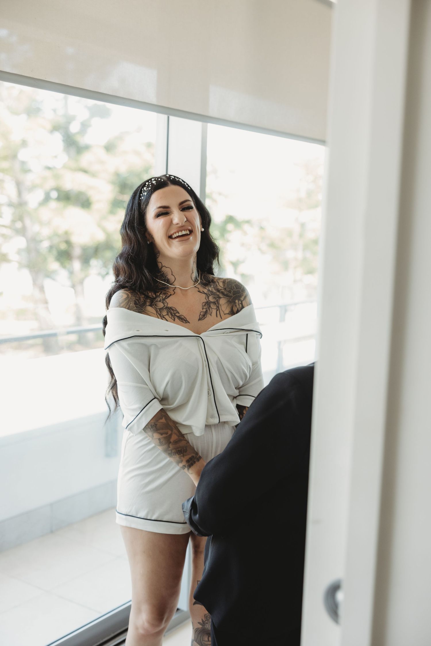 Woman in white loungewear poses playfully against a bright interior space with natural lighting.