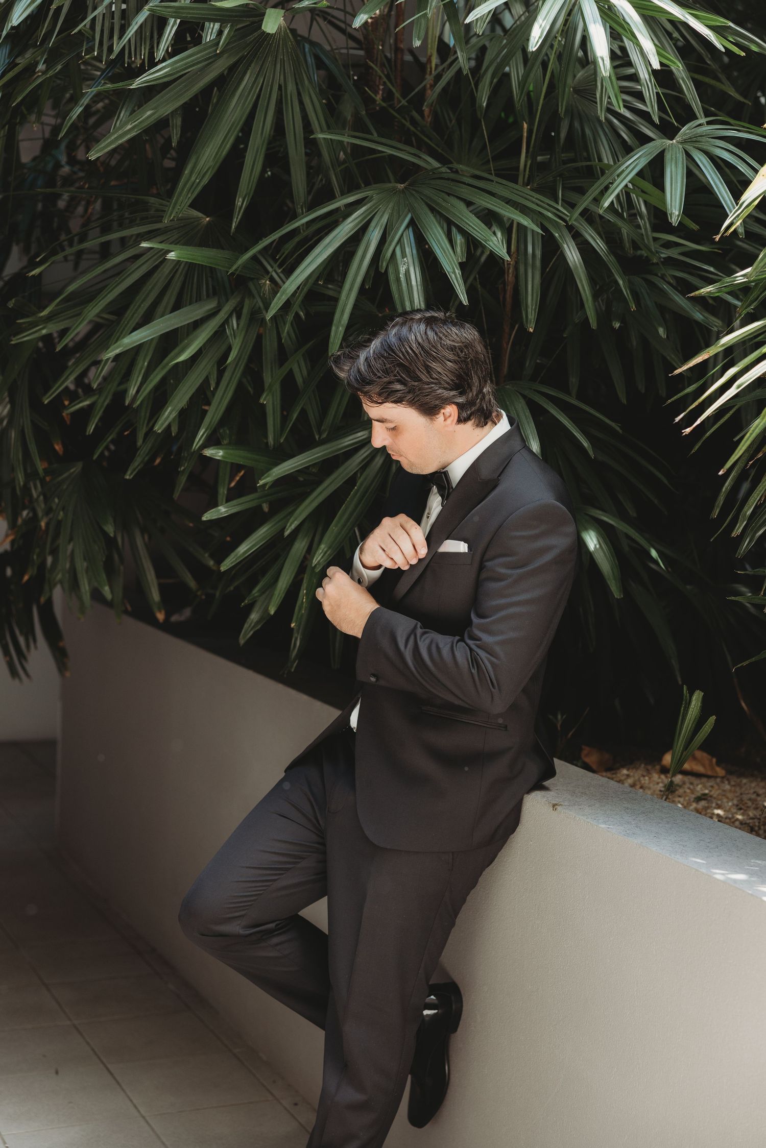 Someone in formal attire poses dramatically among indoor palm plants.