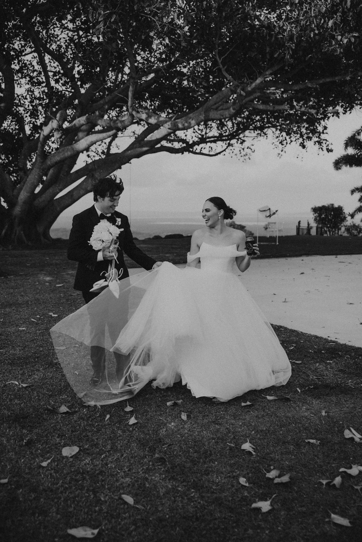 Black and white photo of wedding couple sitting under large tree.