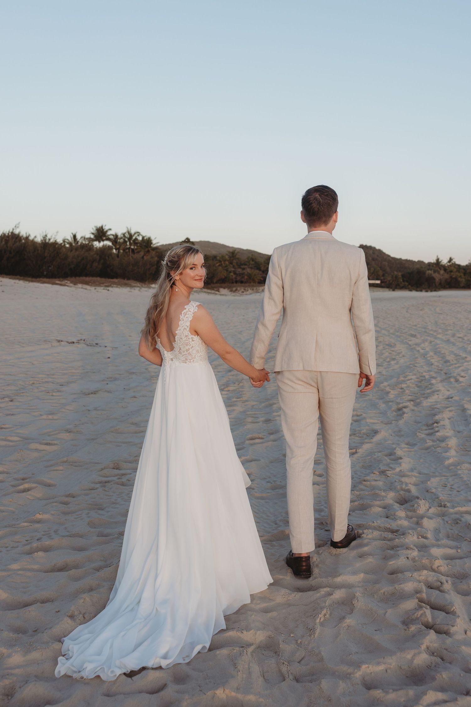A couple walks along the shoreline of a pristine beach during a beautiful sunset.