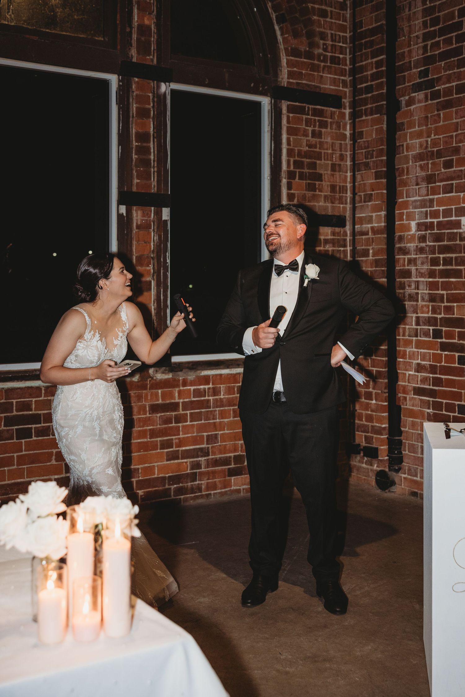 Couple dancing and laughing together during their wedding reception in a rustic brick venue with candlelit decor.