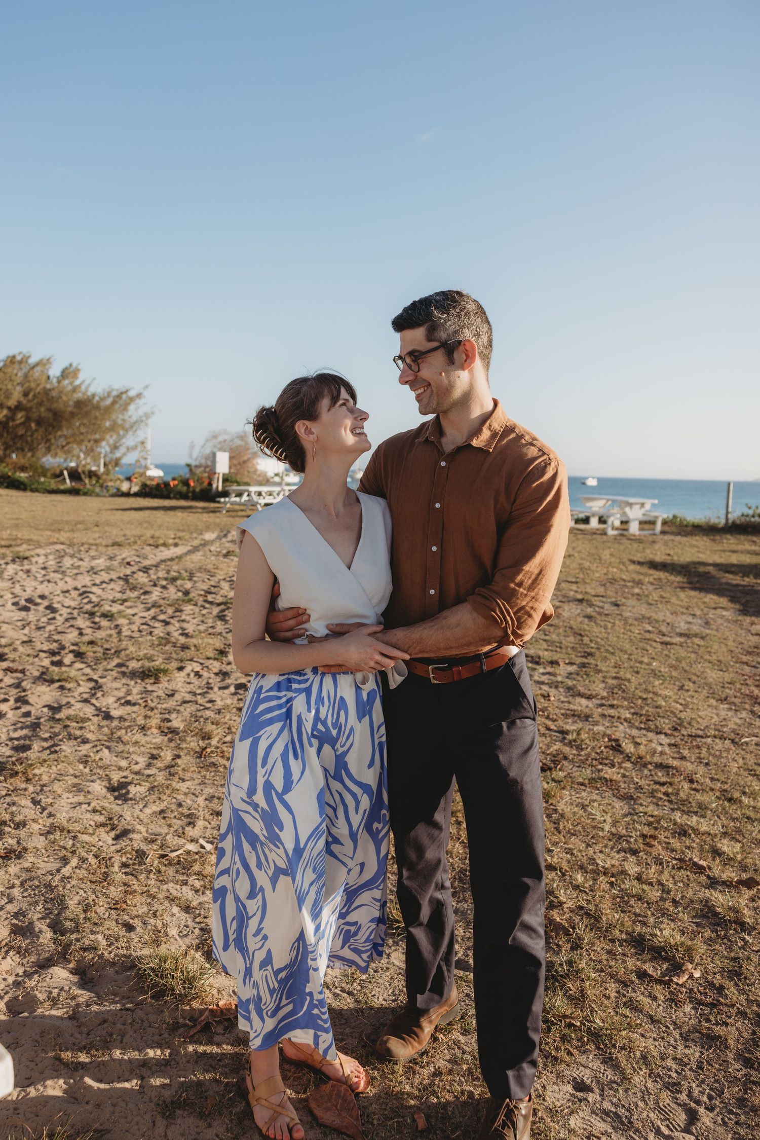 Couple poses together during sunset photoshoot on rocky coastal terrain.