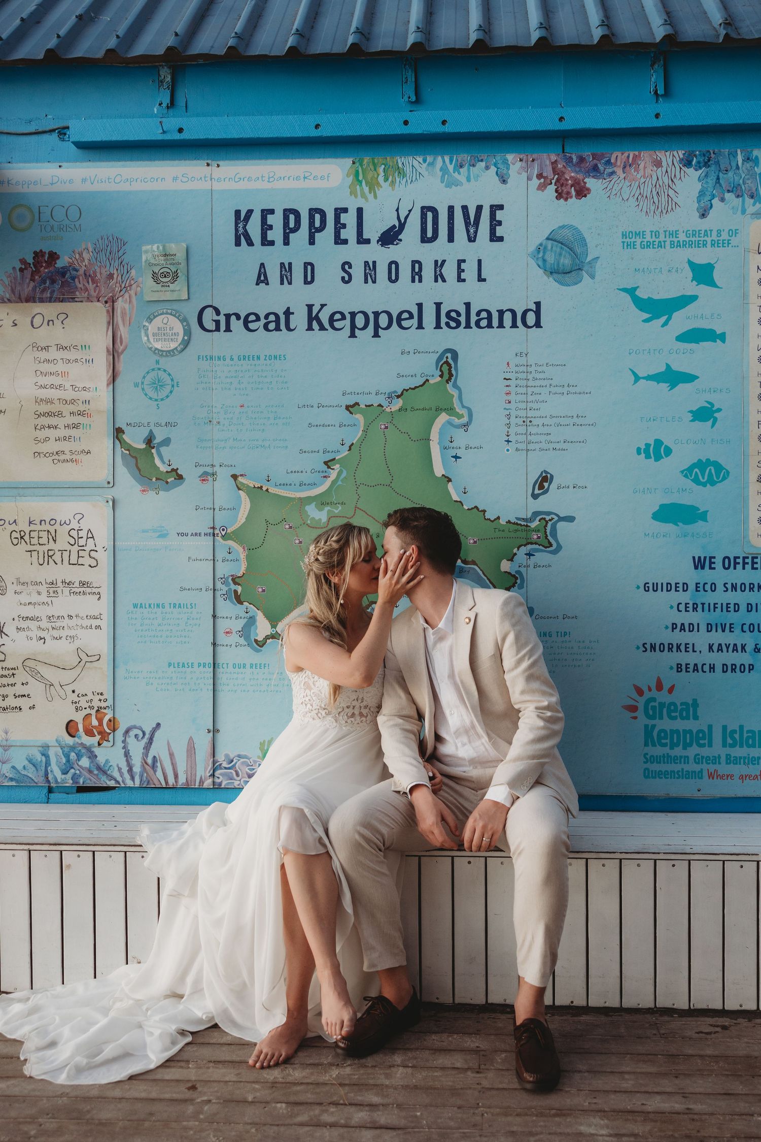 Wedding couple poses playfully against blue wall with nautical maps and beach signage.