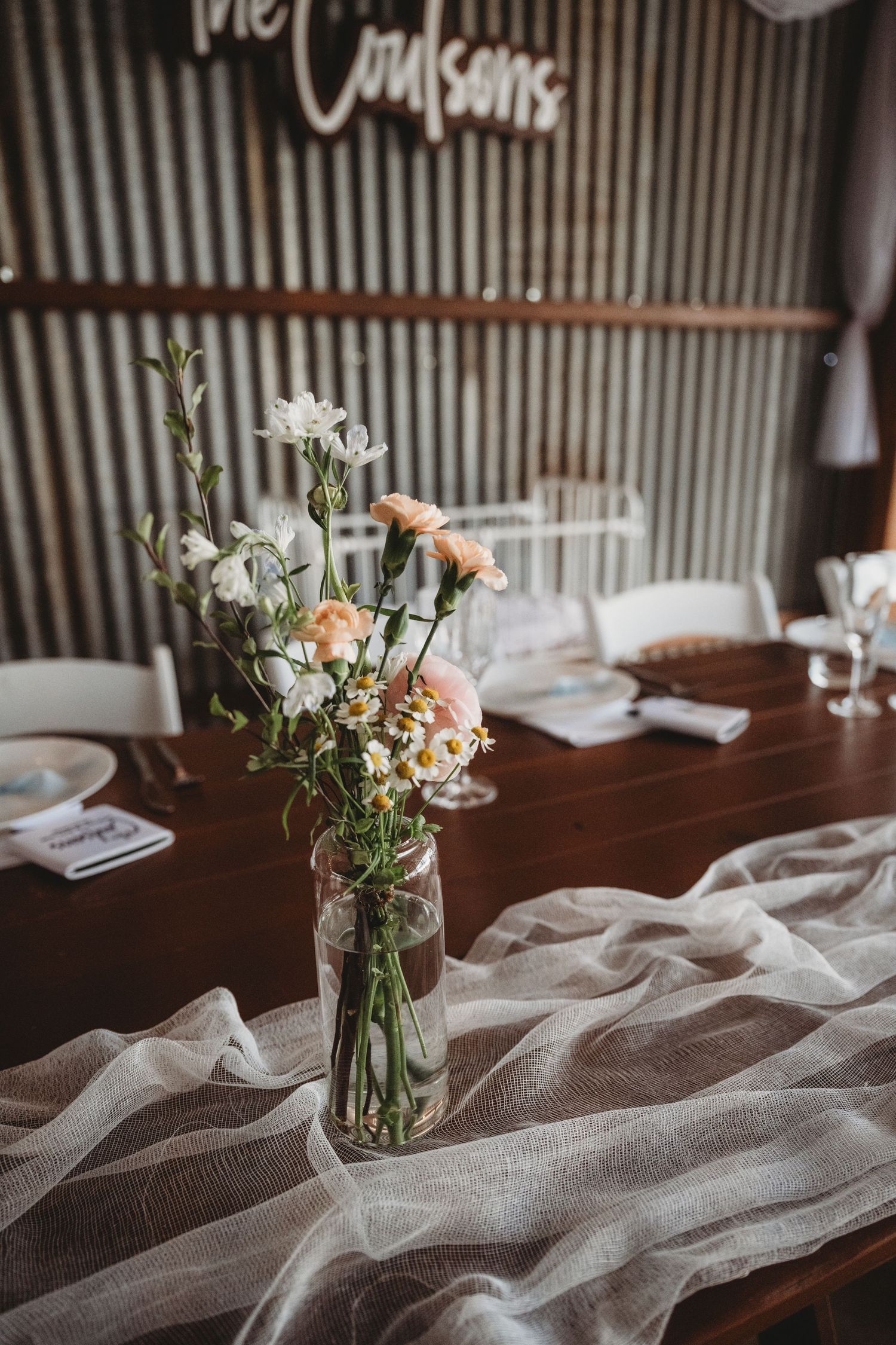 Delicate floral centerpiece with roses in a glass vase on a rustic wooden table with white linen runner.