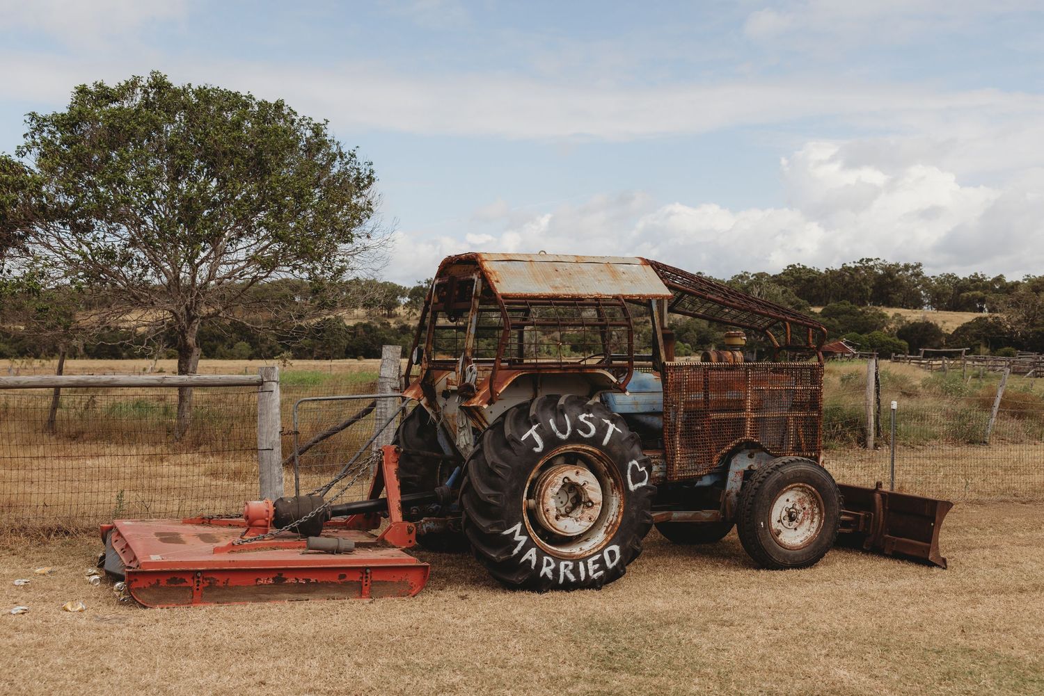 Rustic old tractor with Just Married written on tire at outdoor farm wedding venue.