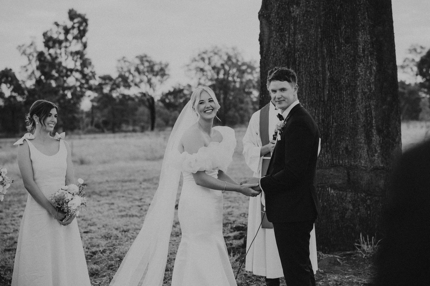 Black and white photograph of a wedding ceremony taking place beneath a majestic tree.