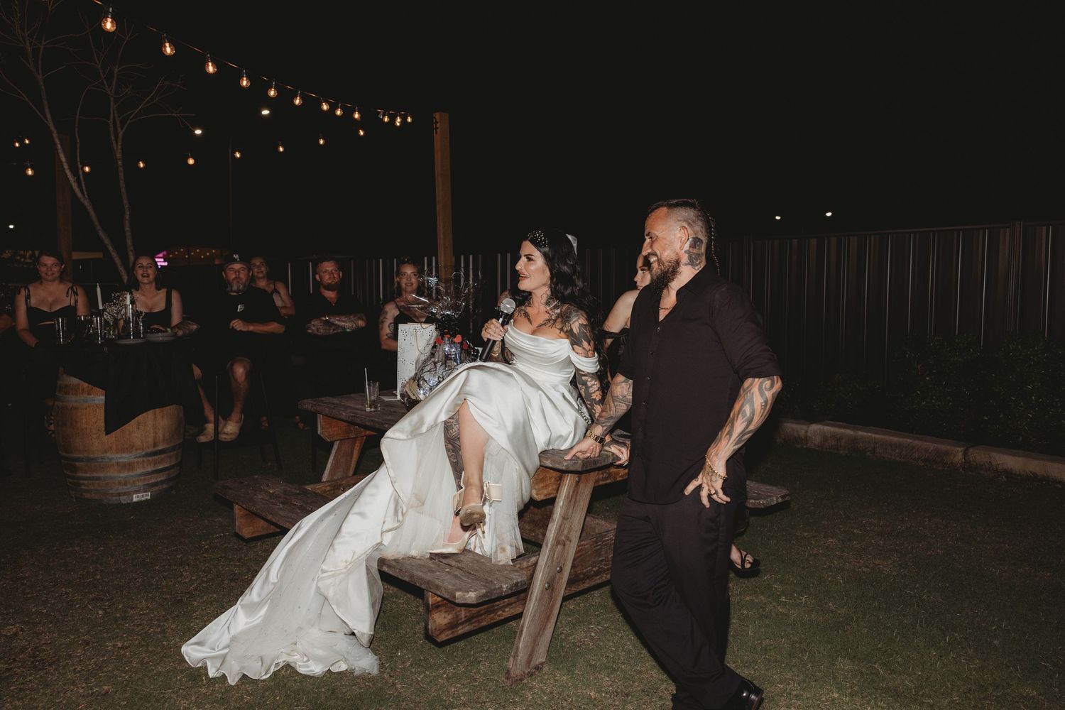A couple shares a romantic dance together under string lights at an outdoor evening wedding reception.