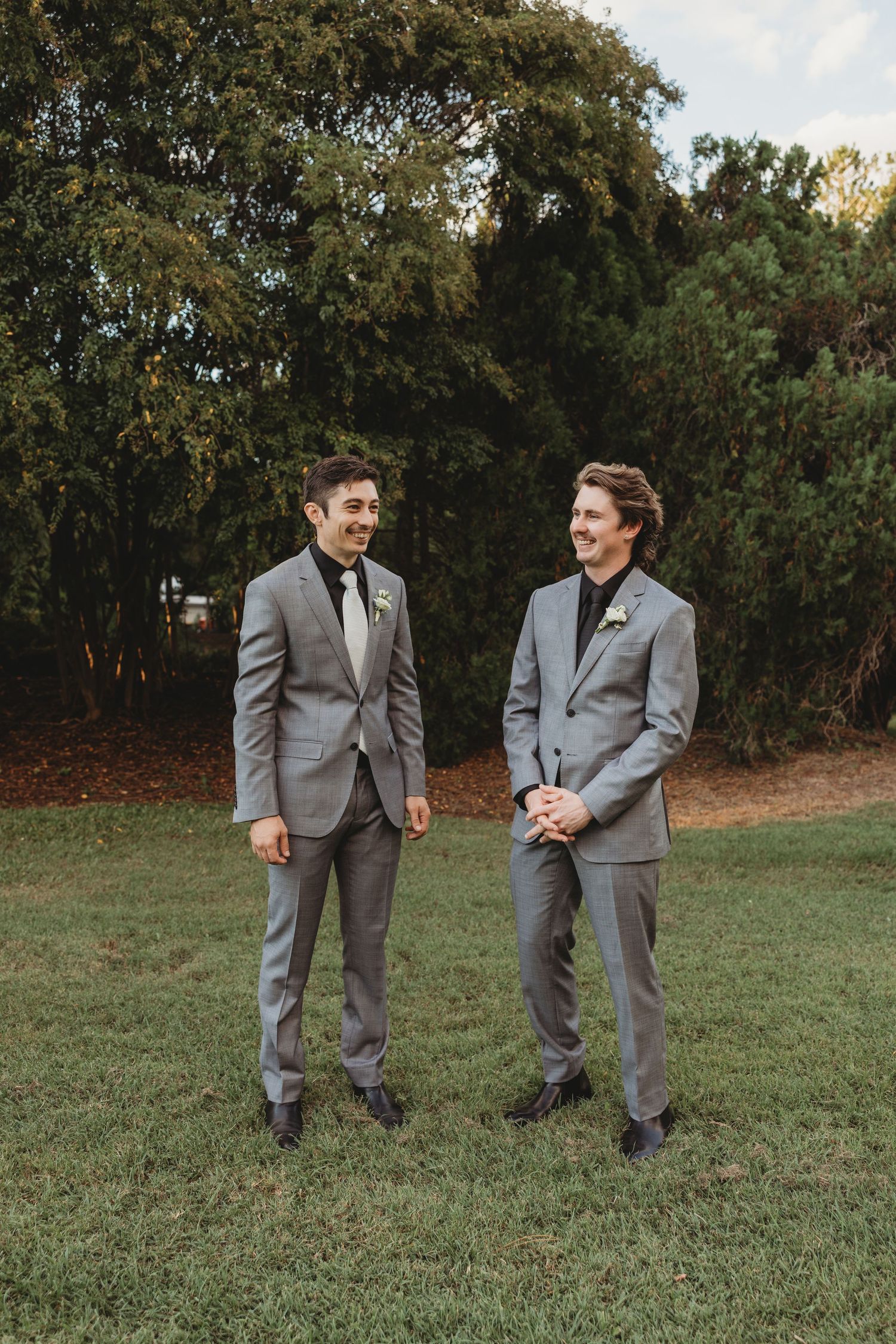 Groomsmen in grey suits share candid moments on grass lawn Rockhampton