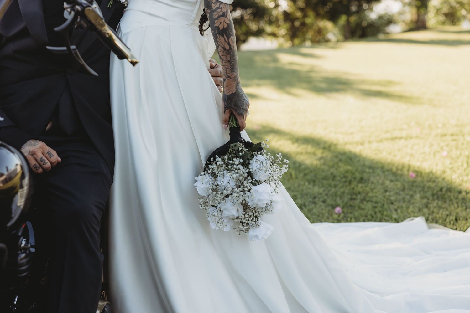 Wedding couple holding delicate white floral bouquet against flowing dress outdoors.