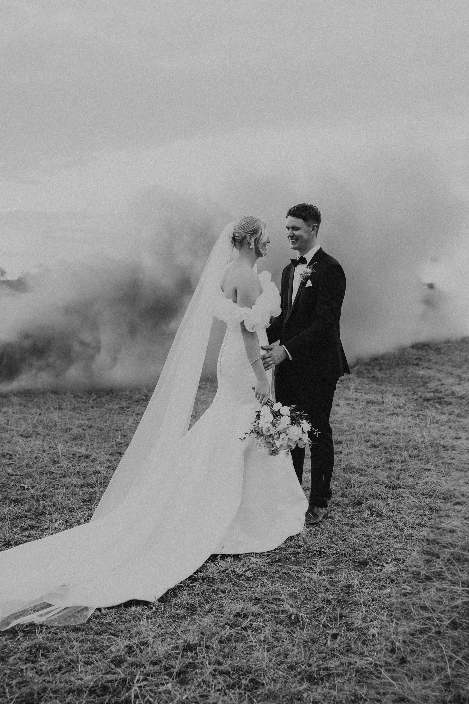 Black and white wedding portraits with atmospheric smoke effects in outdoor field.